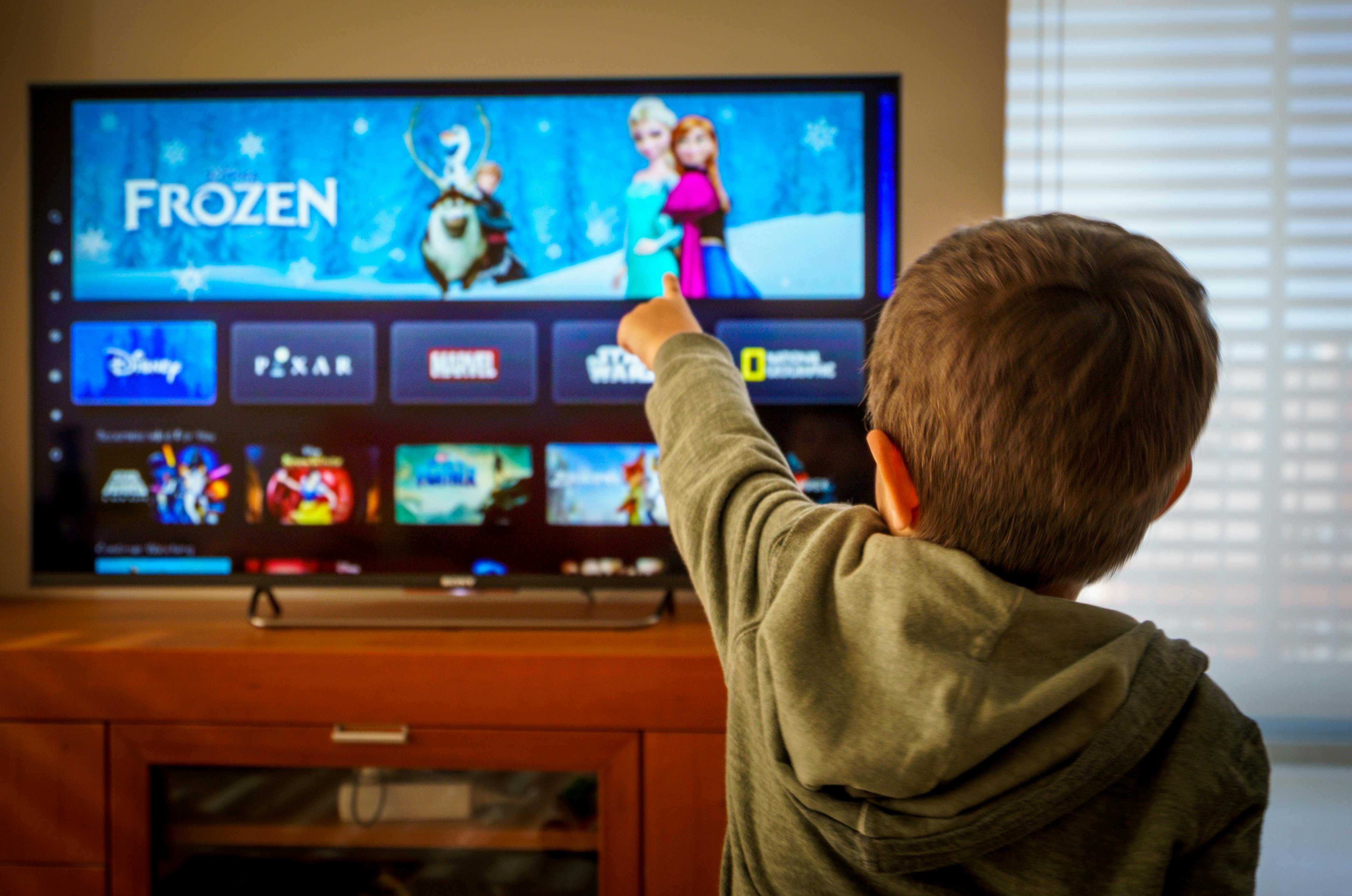 child in living room pointing to Frozen promo on Disney Plus app