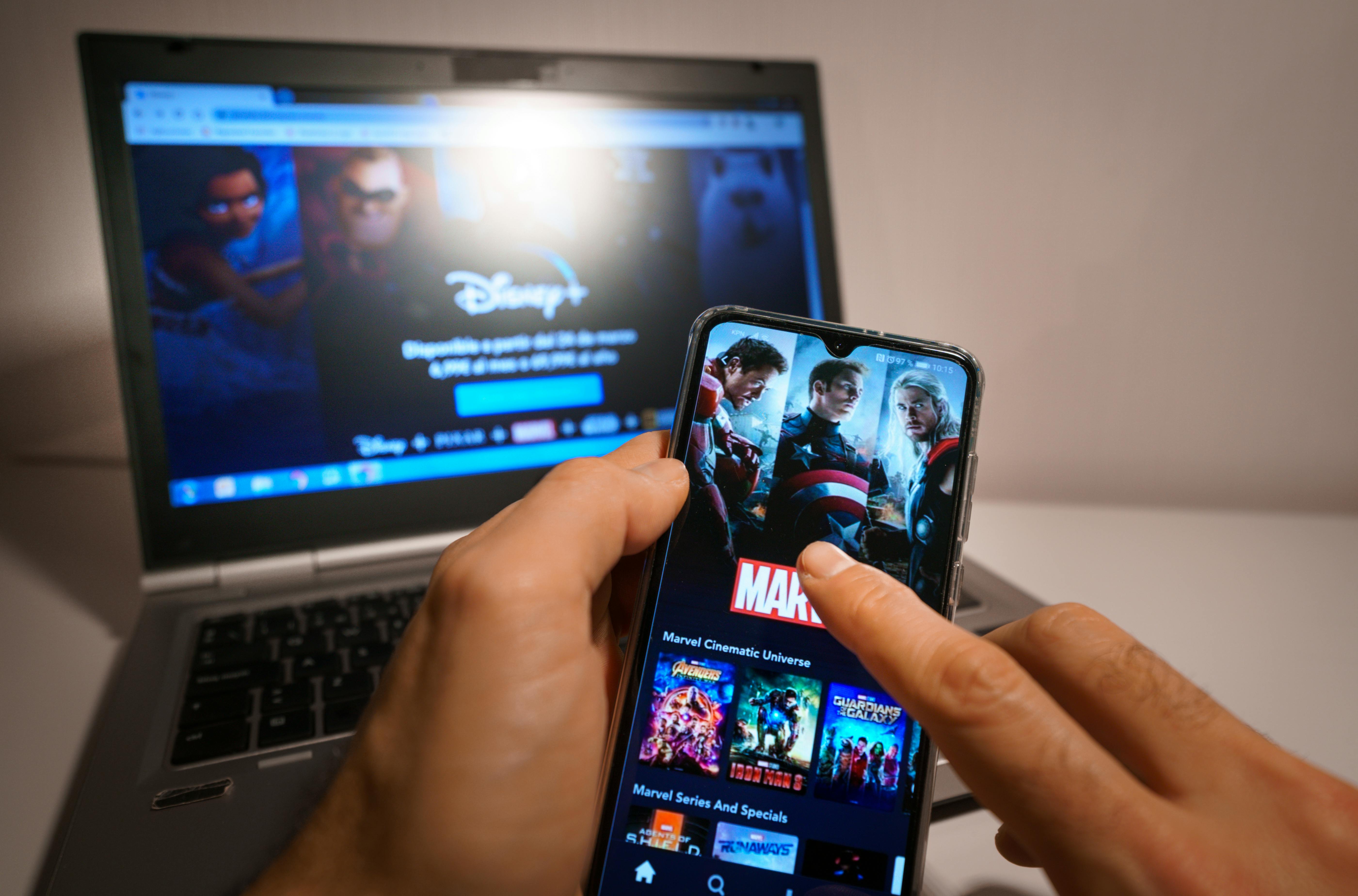 man holding his phone and streaming disney plus on laptop and mobile device