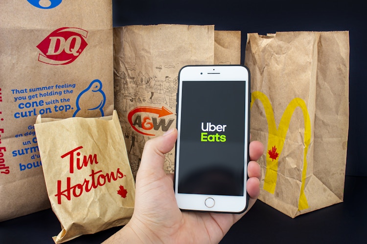 man holding his phone with the uber eats app up next to a bunch of fast food take out bags