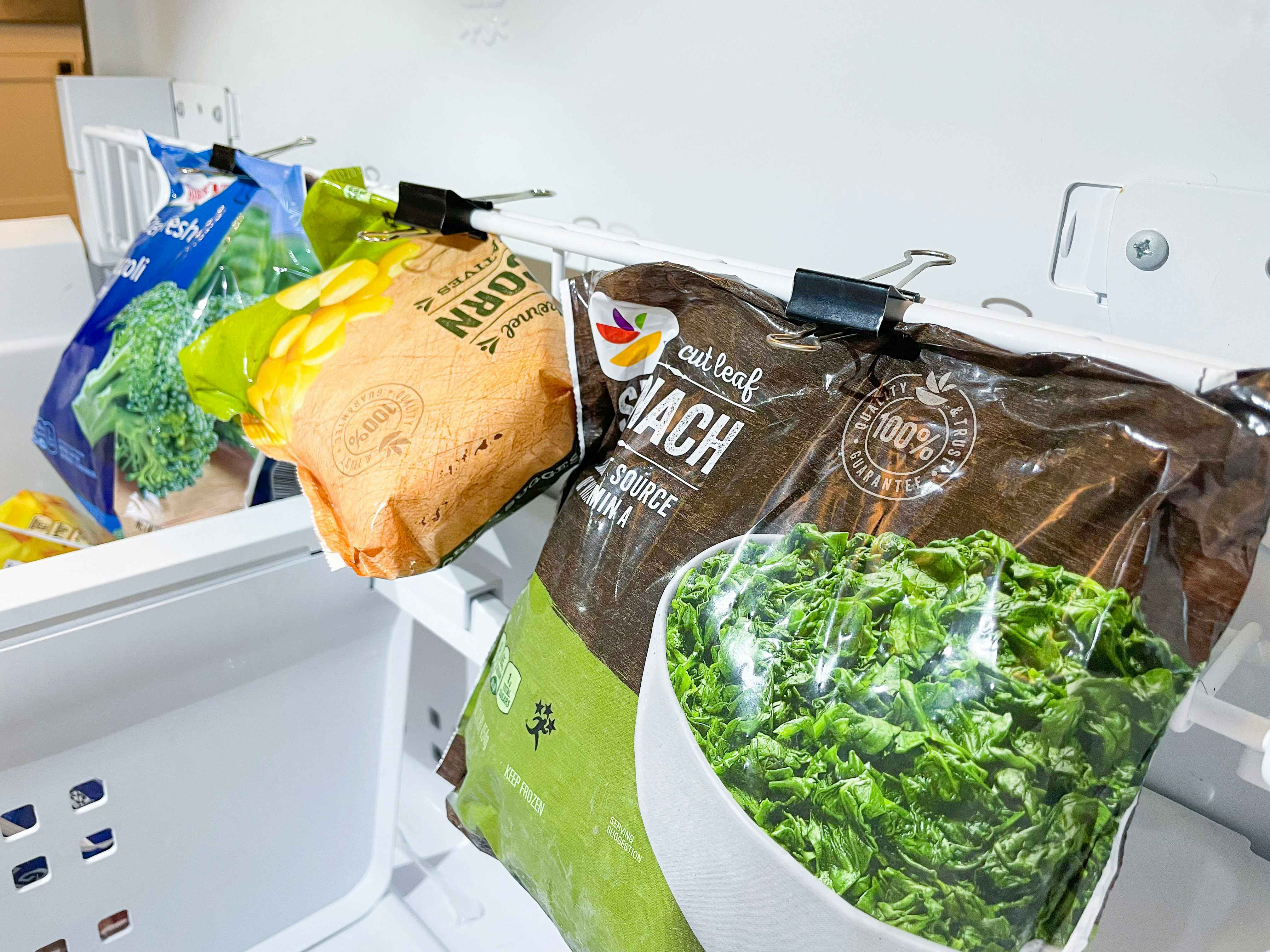 binder clip organization hack showing frozen veggies hanging from binder clips in freezer