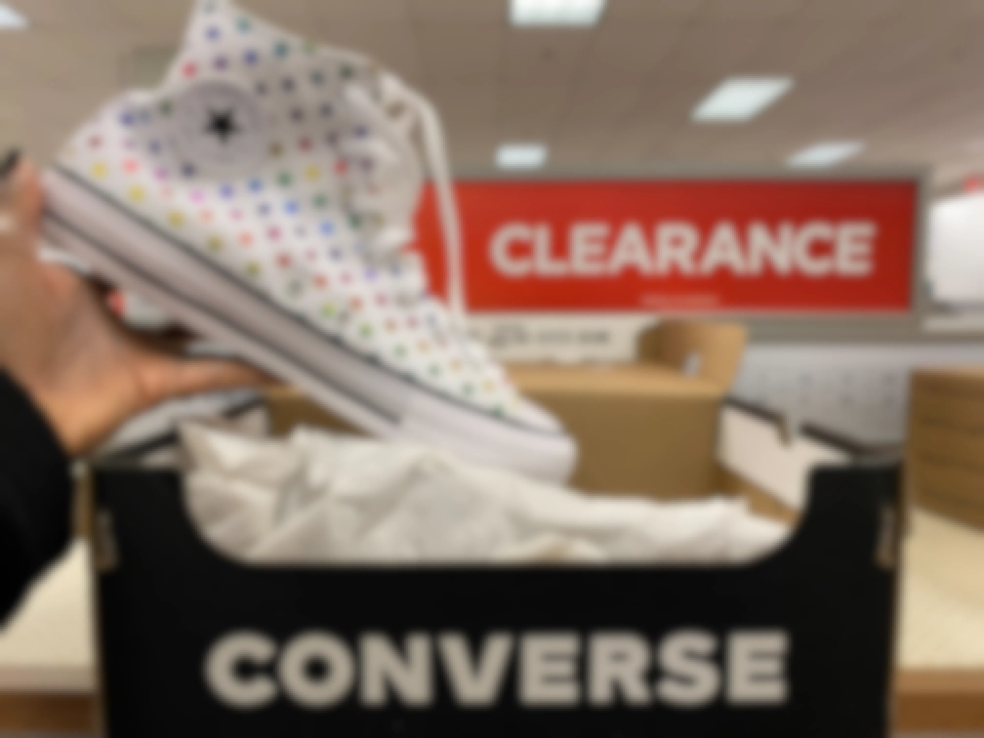 A person's hand holding up a Converse All-Star high-top shoe above its box on a clearance shelf at Kohl's.