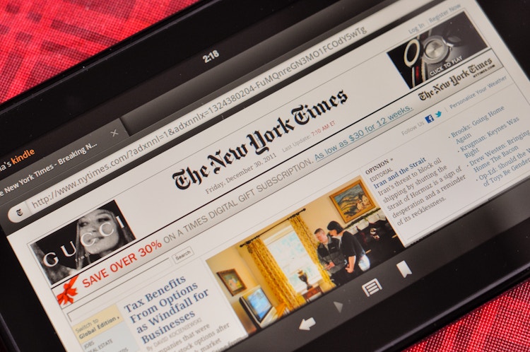 An Amazon Kindle laying on a table displaying The New York Times digital copy front page.