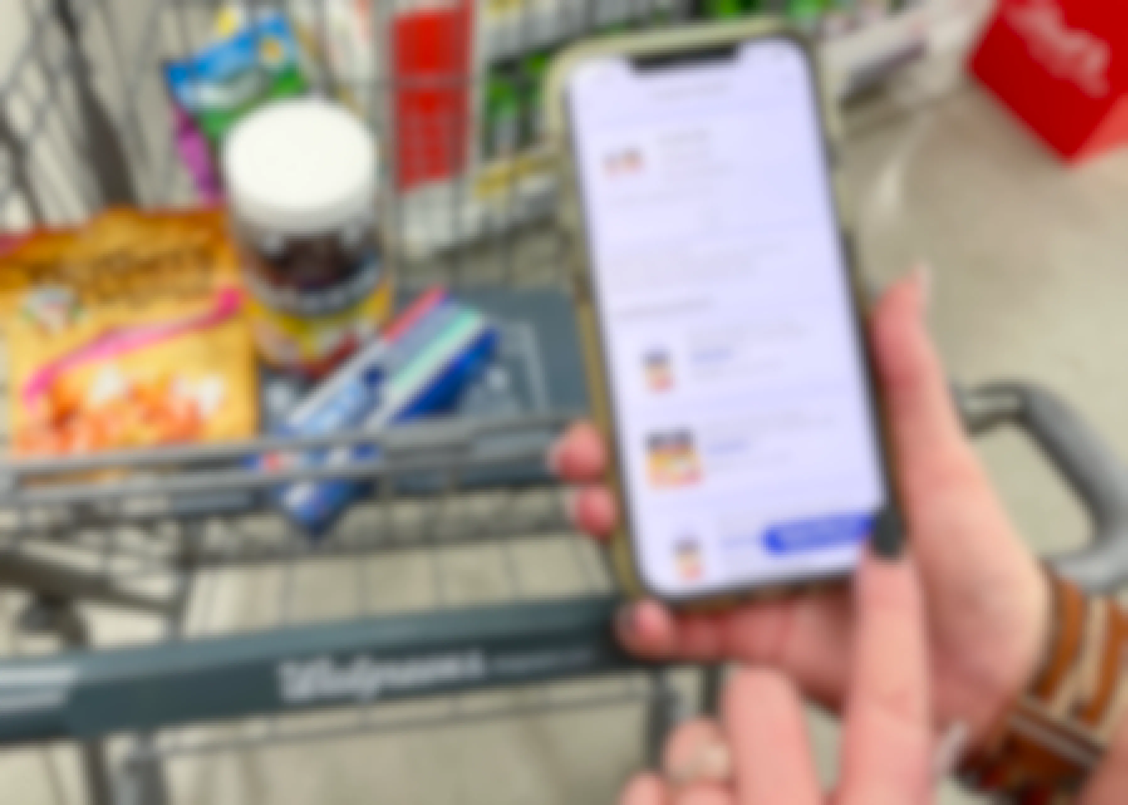 someone holding phone with walgreens app next to cart with candy, vitamins, and toothpaste