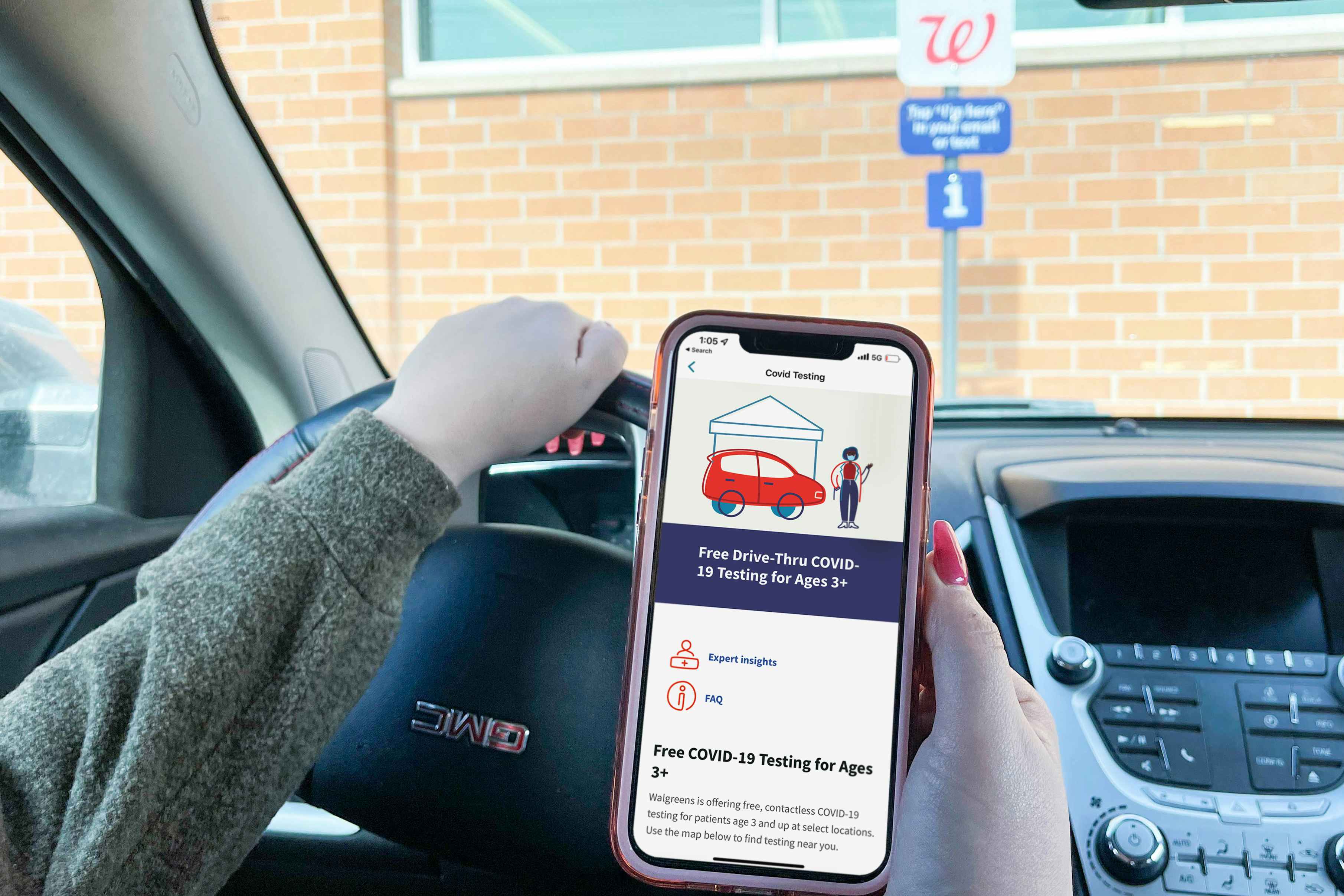 A person sitting in their car, parked in a Walgreens parking lot and holding their phone displaying the drive thru COVID-19 testing information