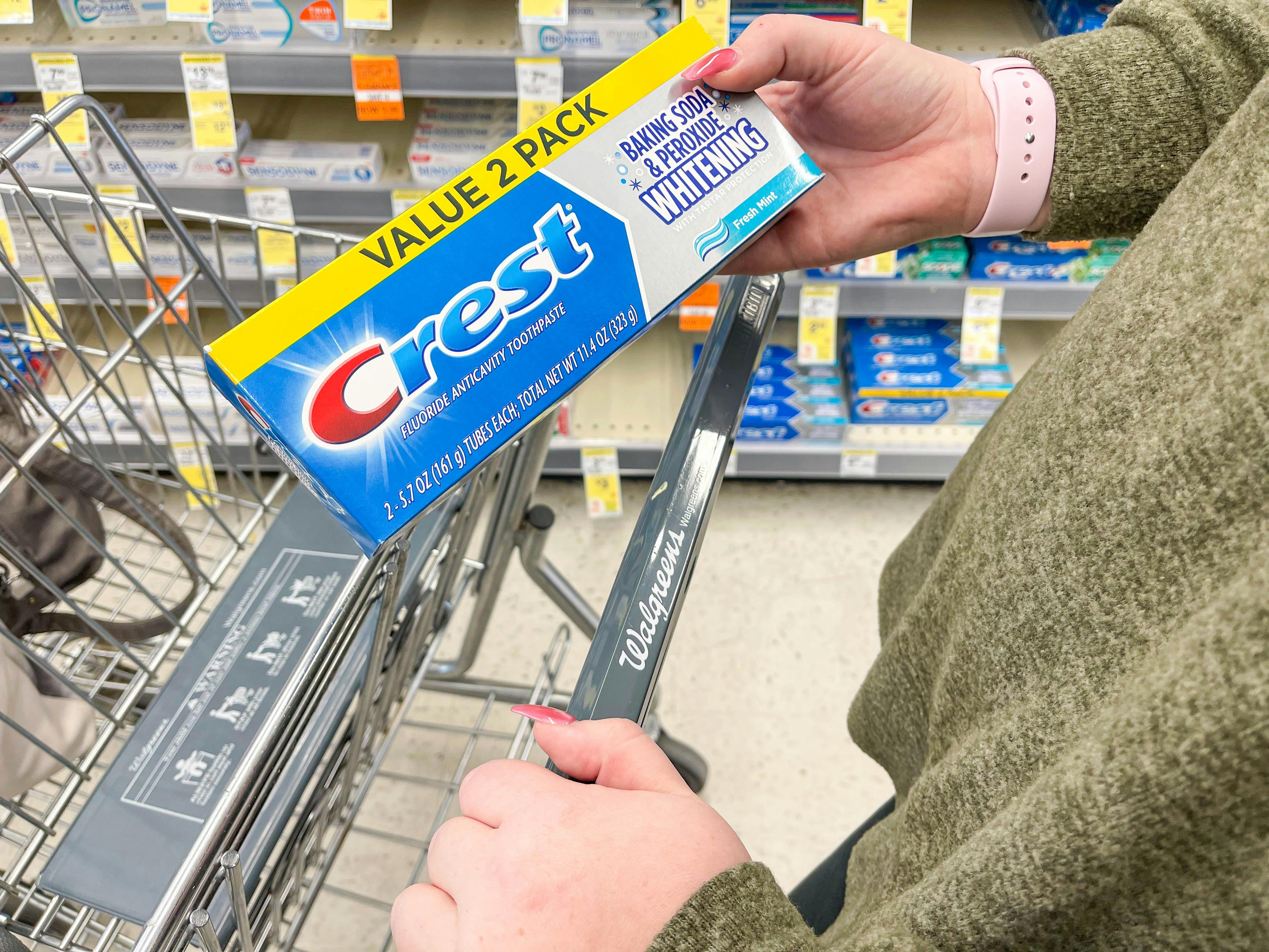 Woman holding Crest toothpaste near a Walgreens cart.