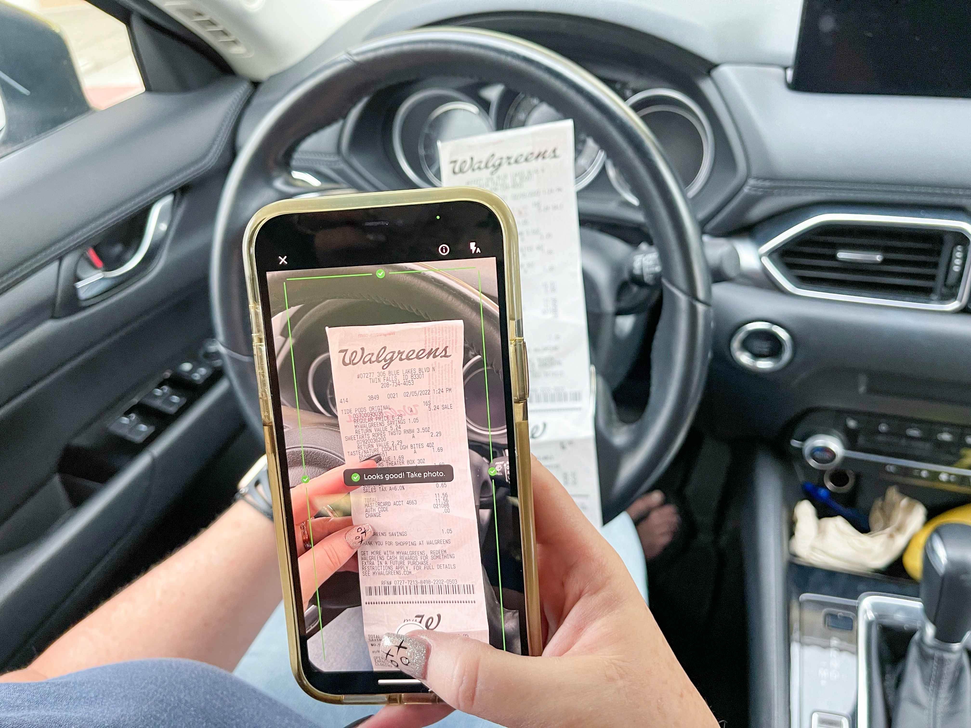 A person sitting in their car and using the receipt-scanning feature on the ibotta app to scan their Walgreens receipt.