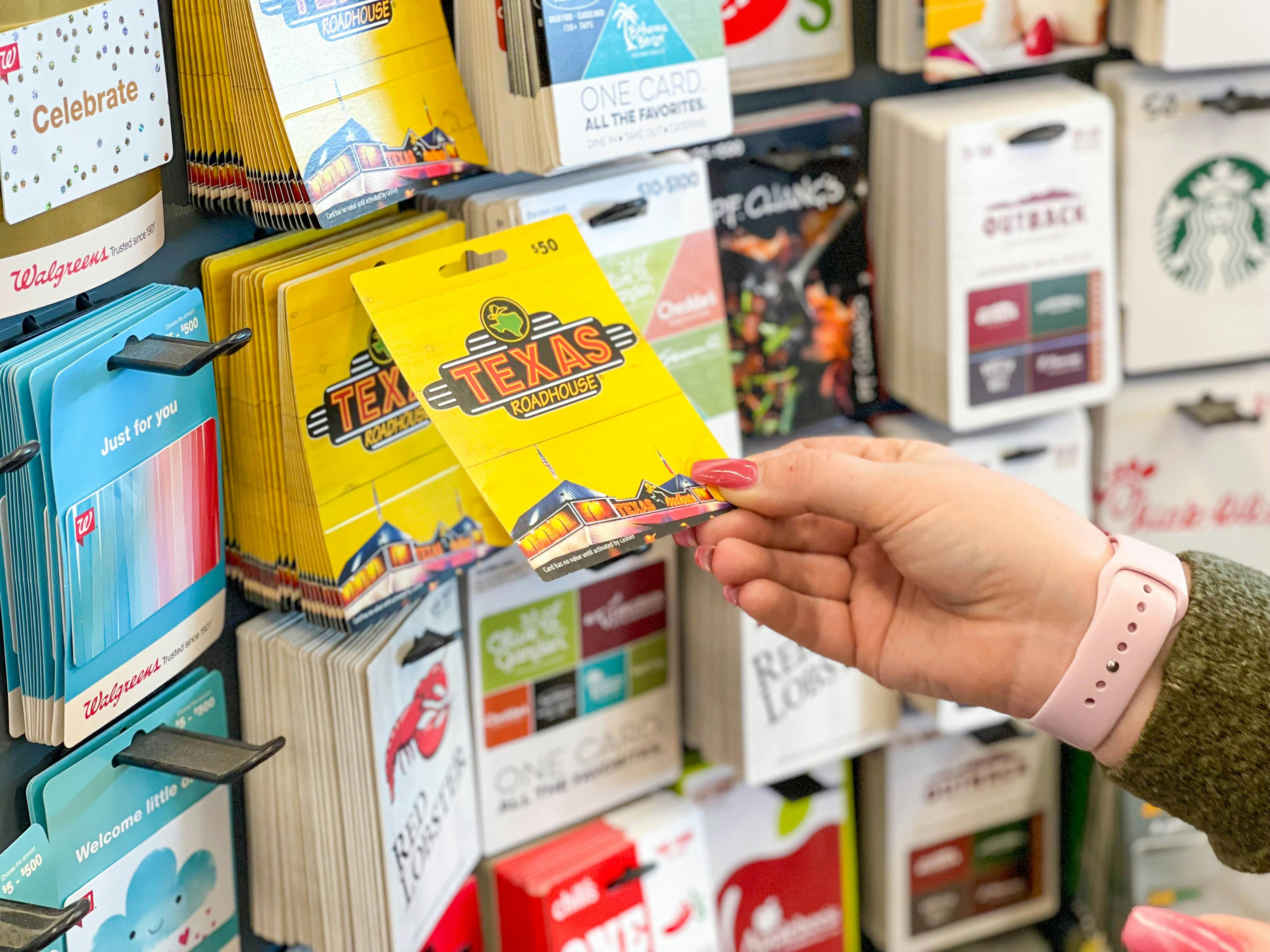 A person reaching to take a gift card from a display of gift cards.