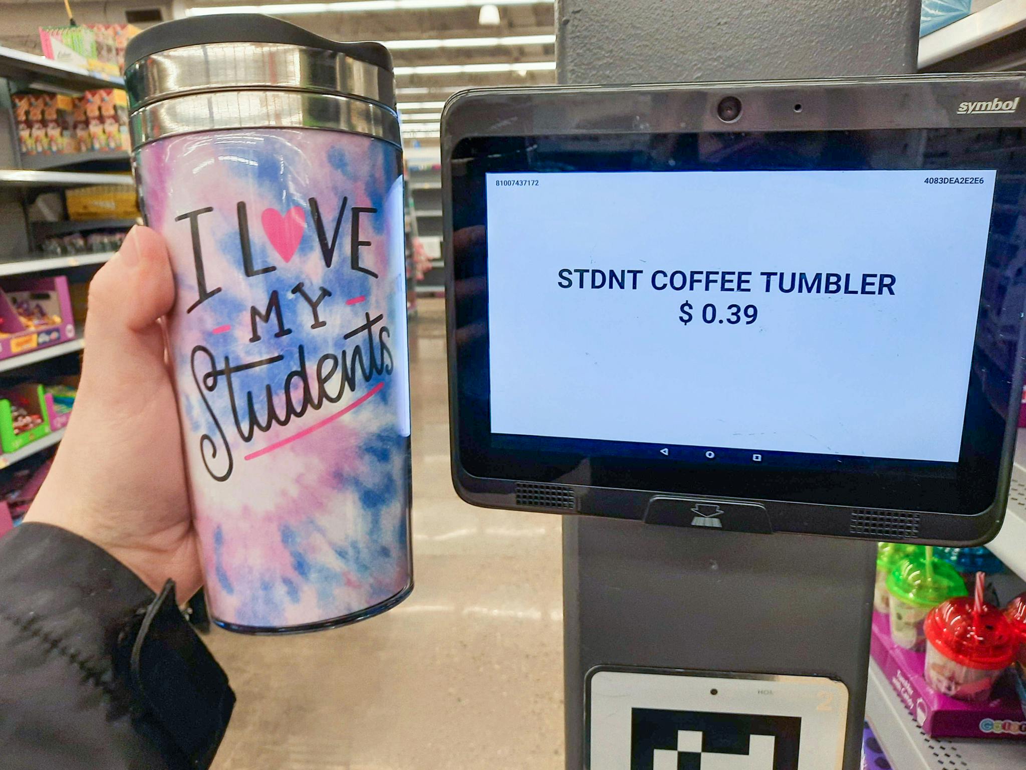 A person's hand holding up a coffee tumbler next to a price scanner in Walmart which shows the price to be 39 cents.