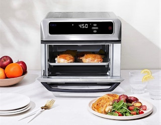 A Chefman air fryer toaster oven cooking chicken near a plate of food.