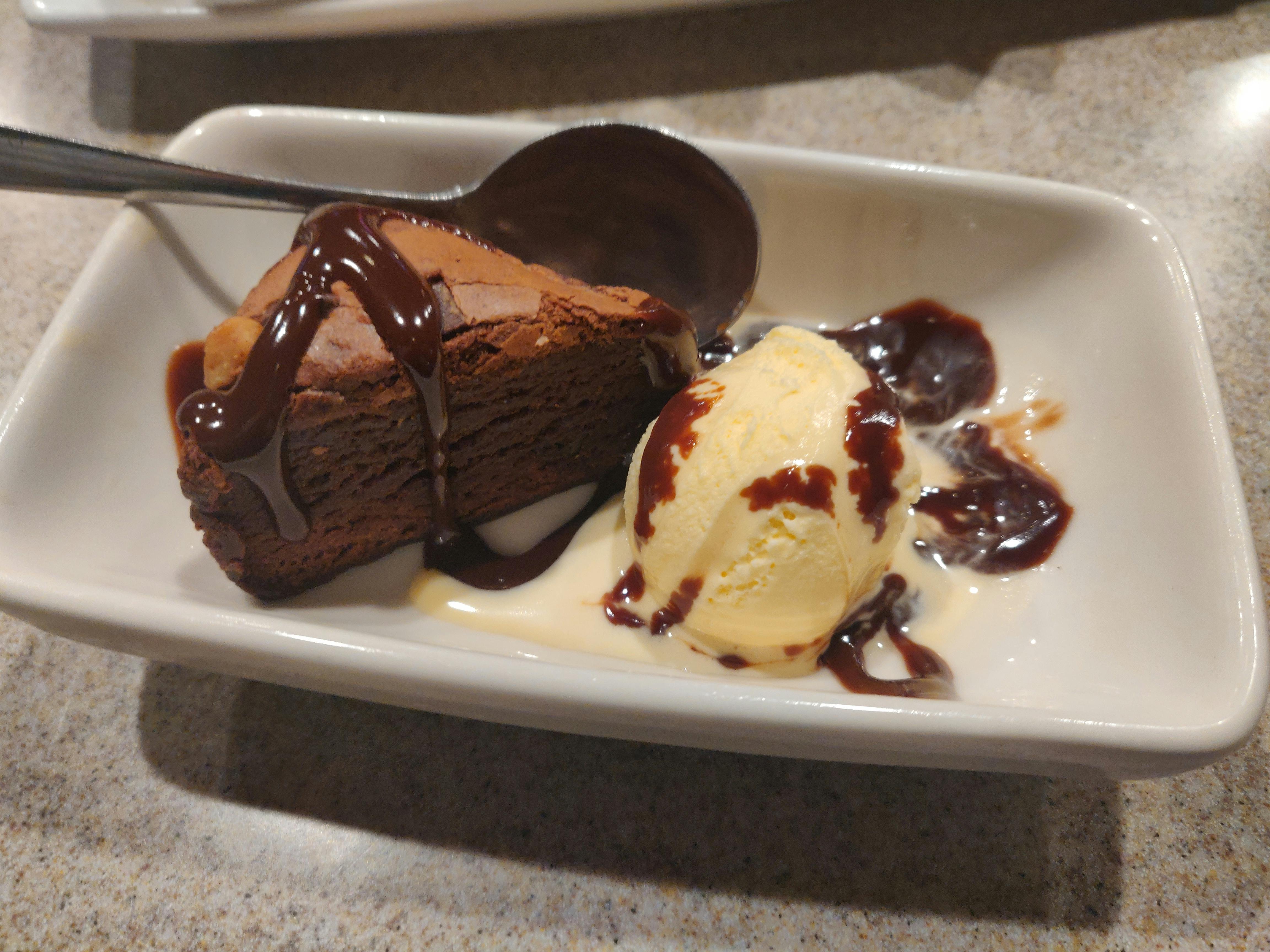 An Applebee's brownie dessert with ice cream and chocolate sauce on a plate with a spoon.