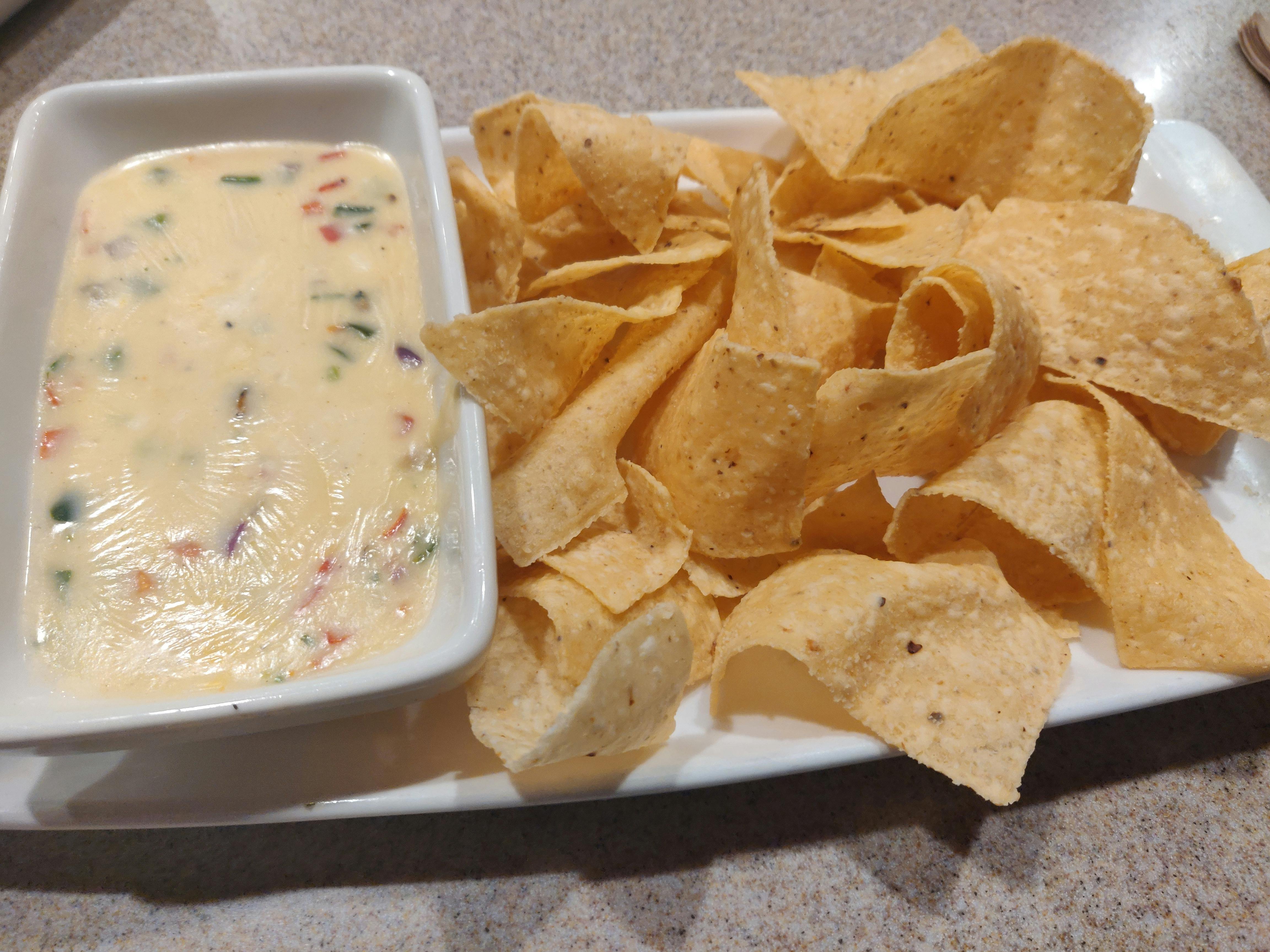 A plate of tortilla chips and a bowl of queso dip sitting on a table at Applebee's.