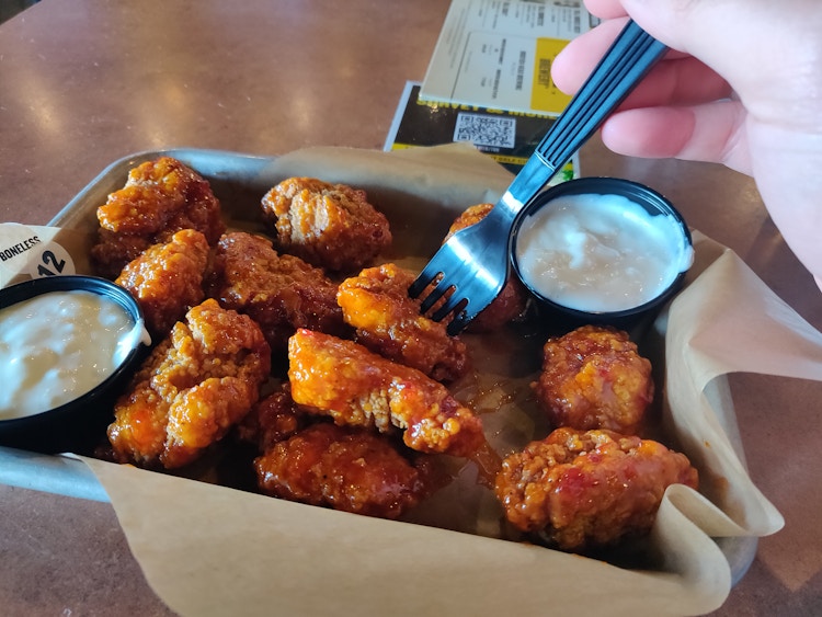 person putting their fork into buffalo wild wings boneless wings.