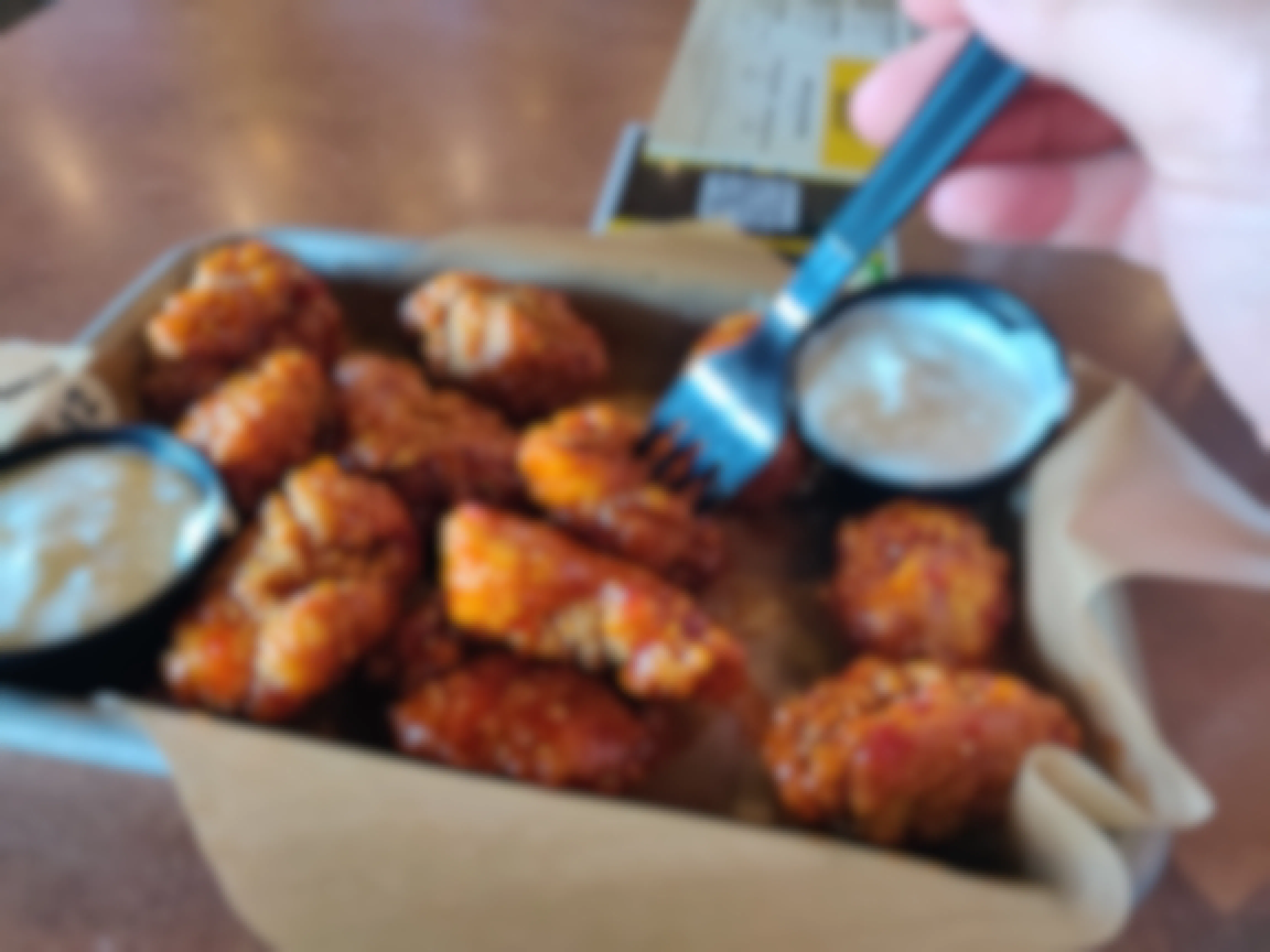 A person using a fork to pick up a boneless wing out of a platter of boneless wings and two dip cups.