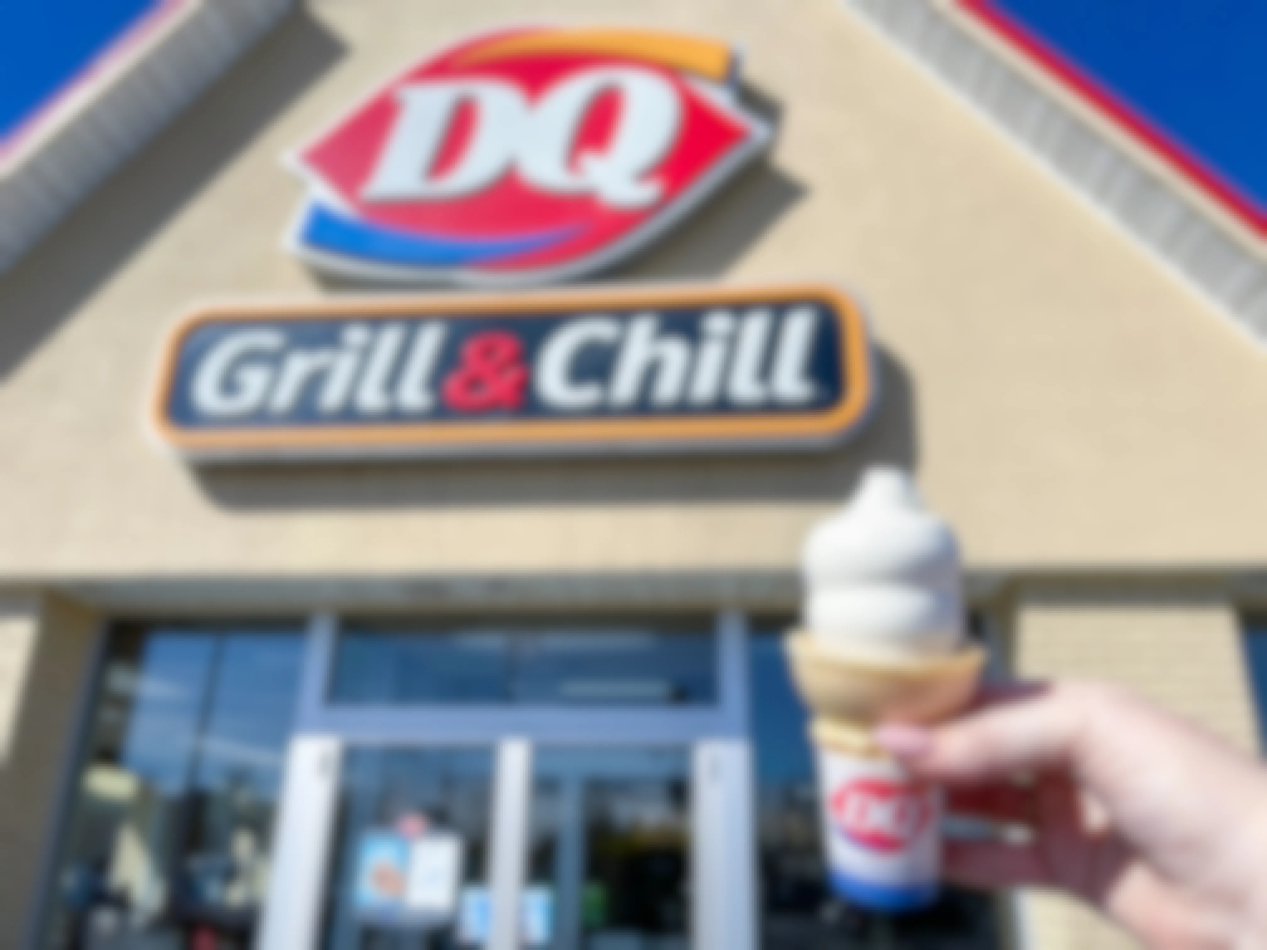 Someone holding a Dairy Queen soft serve cone in front of a Dairy Queen storefront.