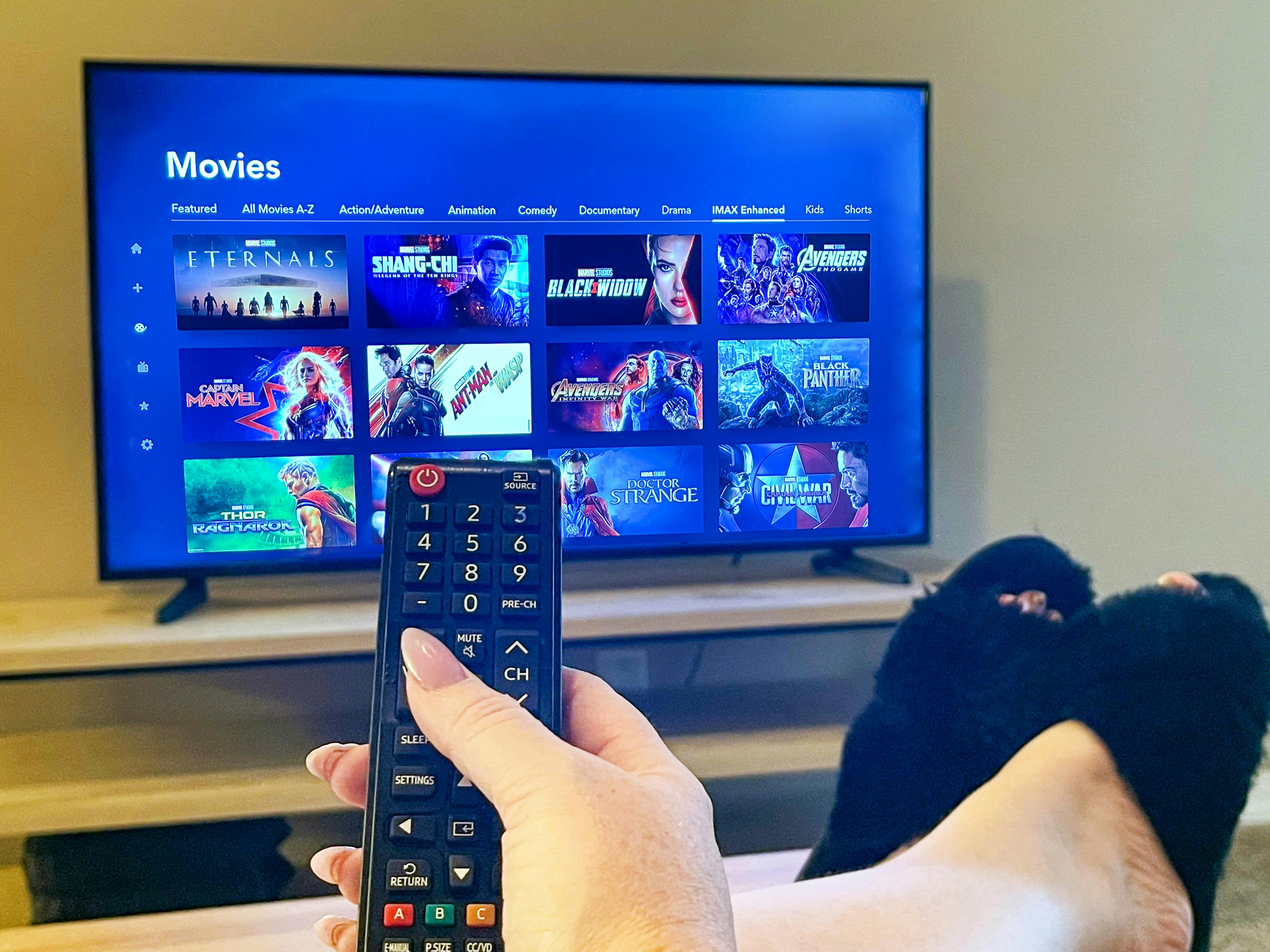 woman holding remote and watching Disney Plus movies on tv