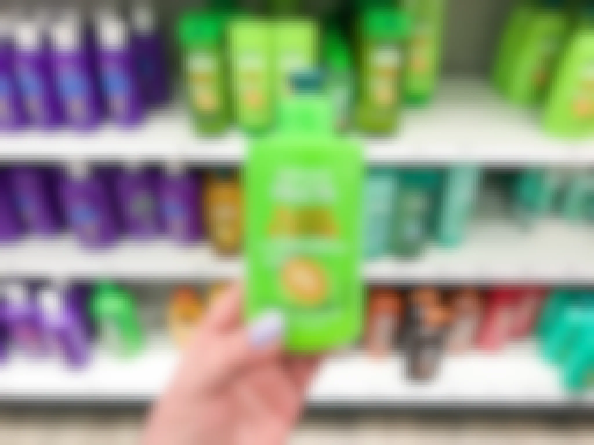 A person's hand holding up a bottle of Garnier Fructis Sleek & Shine Leave-in Conditioner in front of a shelf of haircare products at Target.