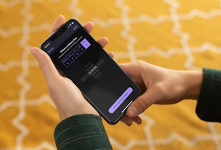 - A person holding an iPhone that is displaying the Grubhub mobile app's scheduling page. The user is setting up a delivery for a future time and date.