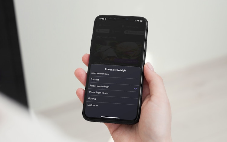 A person holding their iPhone with the Grubhub mobile app open to the sort-by options. The options read, 