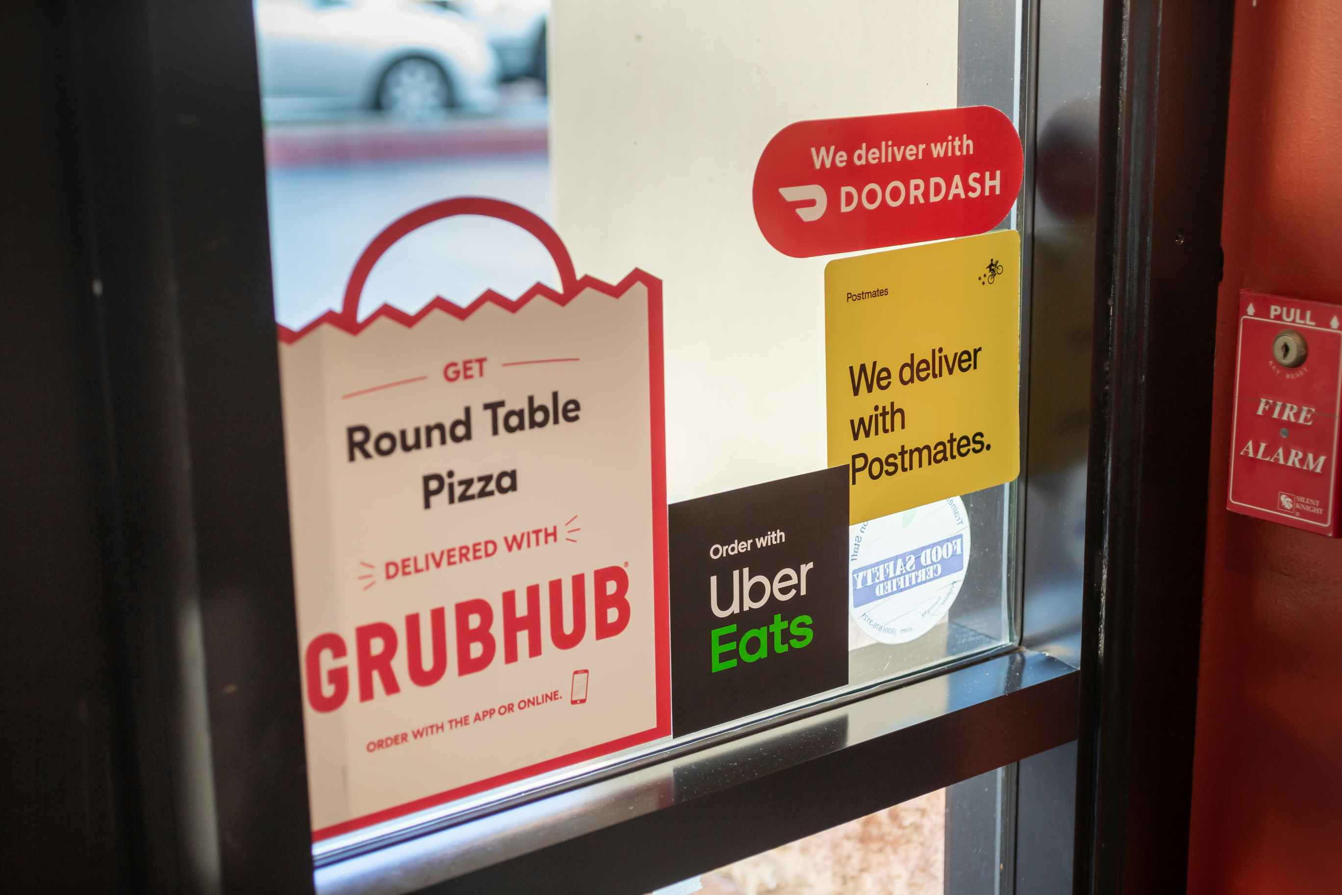 - A restaurant window displaying stickers for various food delivery services, including Grubhub, Uber Eats, Postmates, and Doordash.