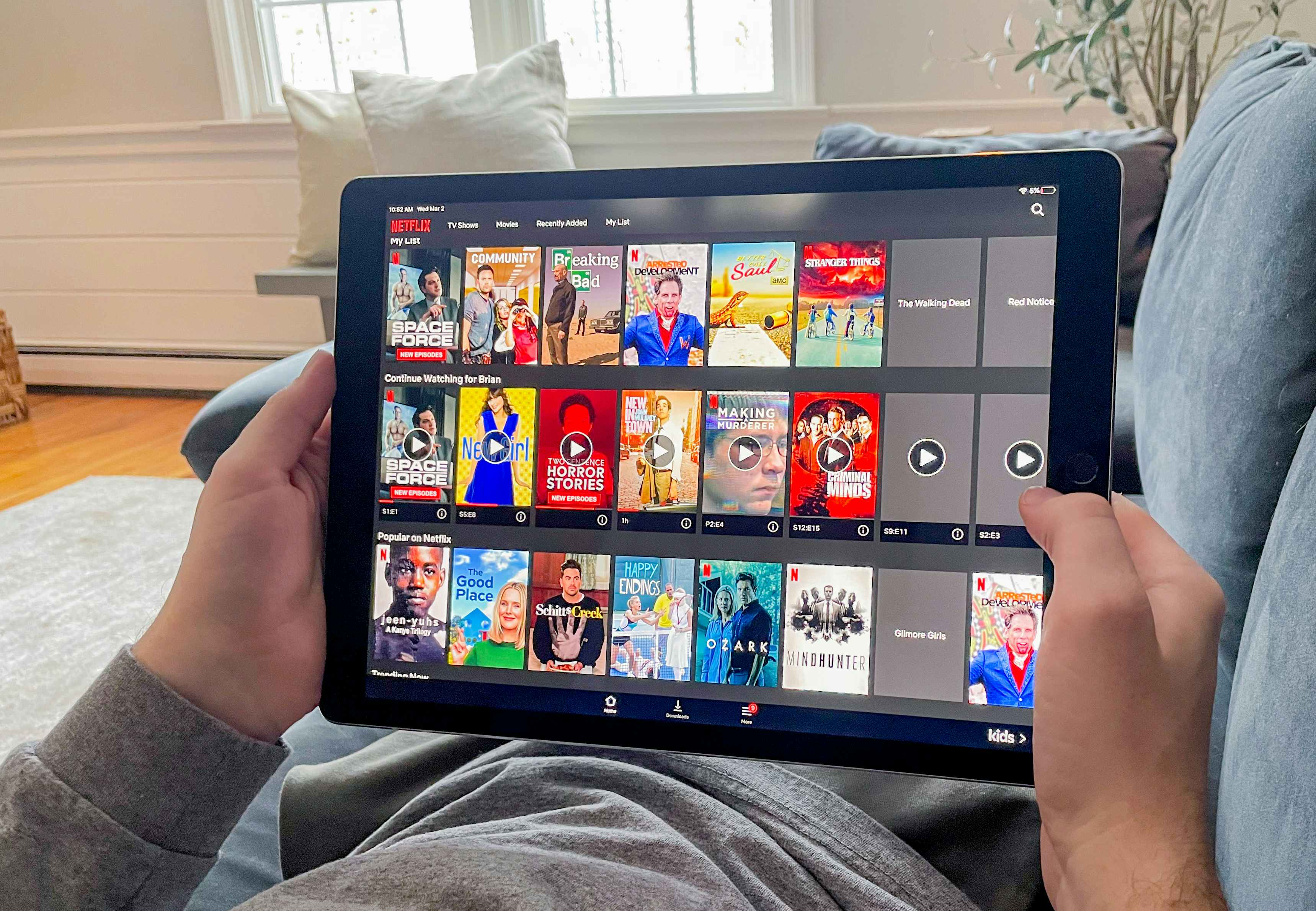 man laying on couch watching netflix through the app on his tablet