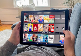 man laying on couch watching netflix through the app on his tablet