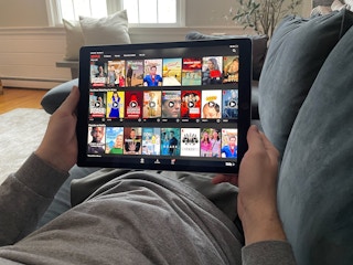 man laying on couch watching netflix through the app on his tablet