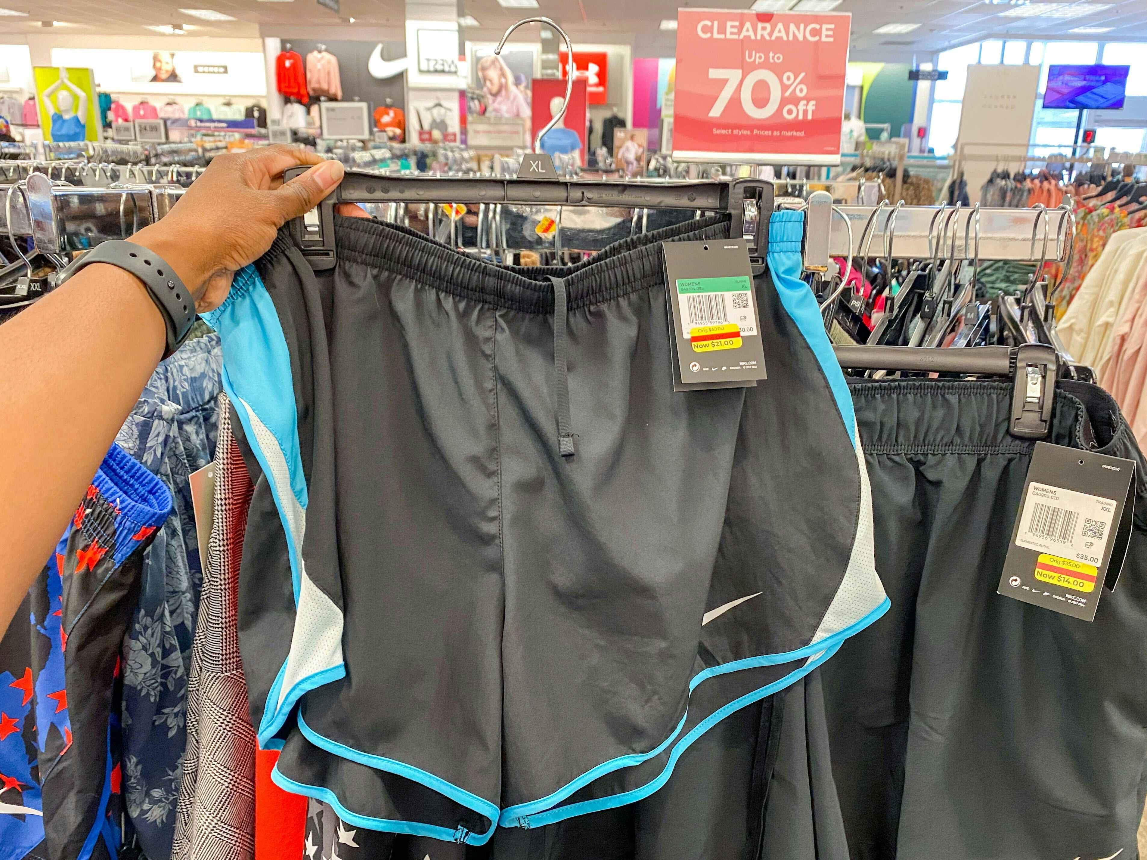 Hand holding up grey athletic shorts next to a clearance sign inside a Kohl's