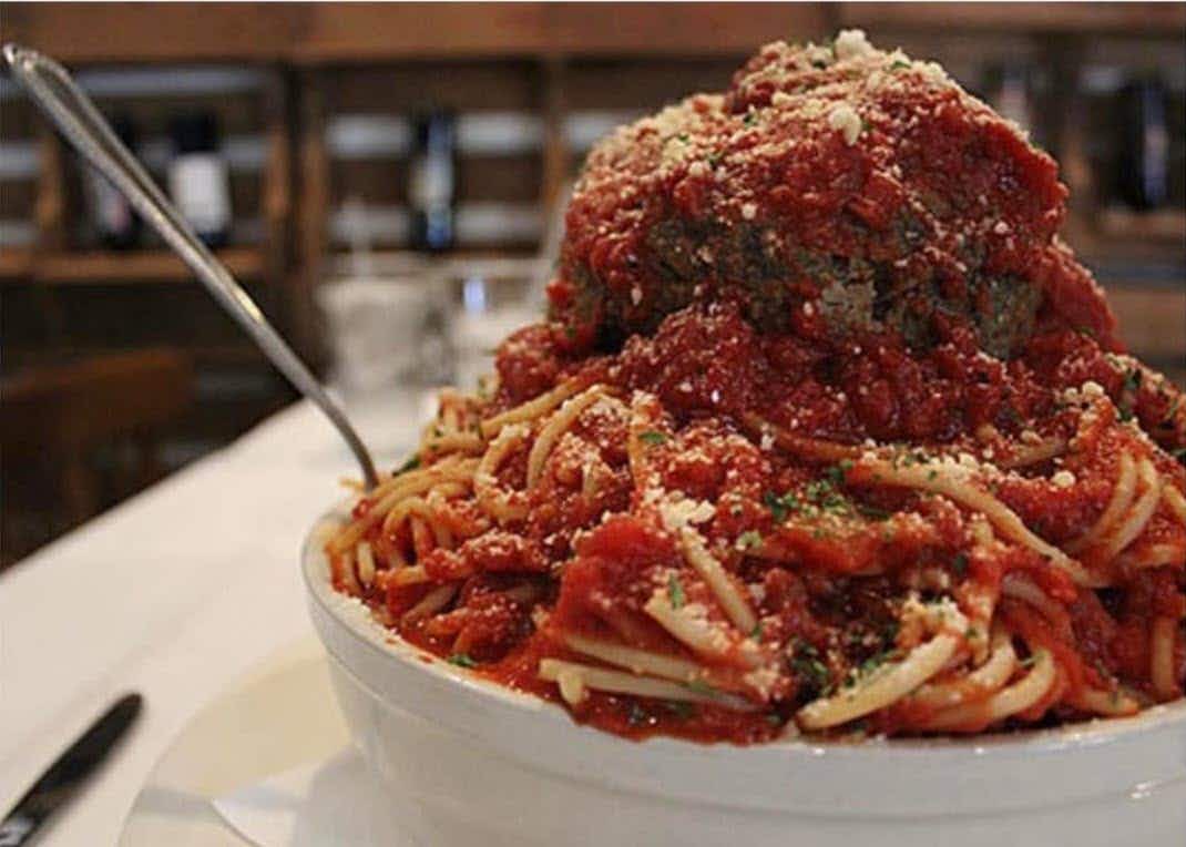 A bowl with spaghetti and a giant meatball on top with spaghetti sauce.