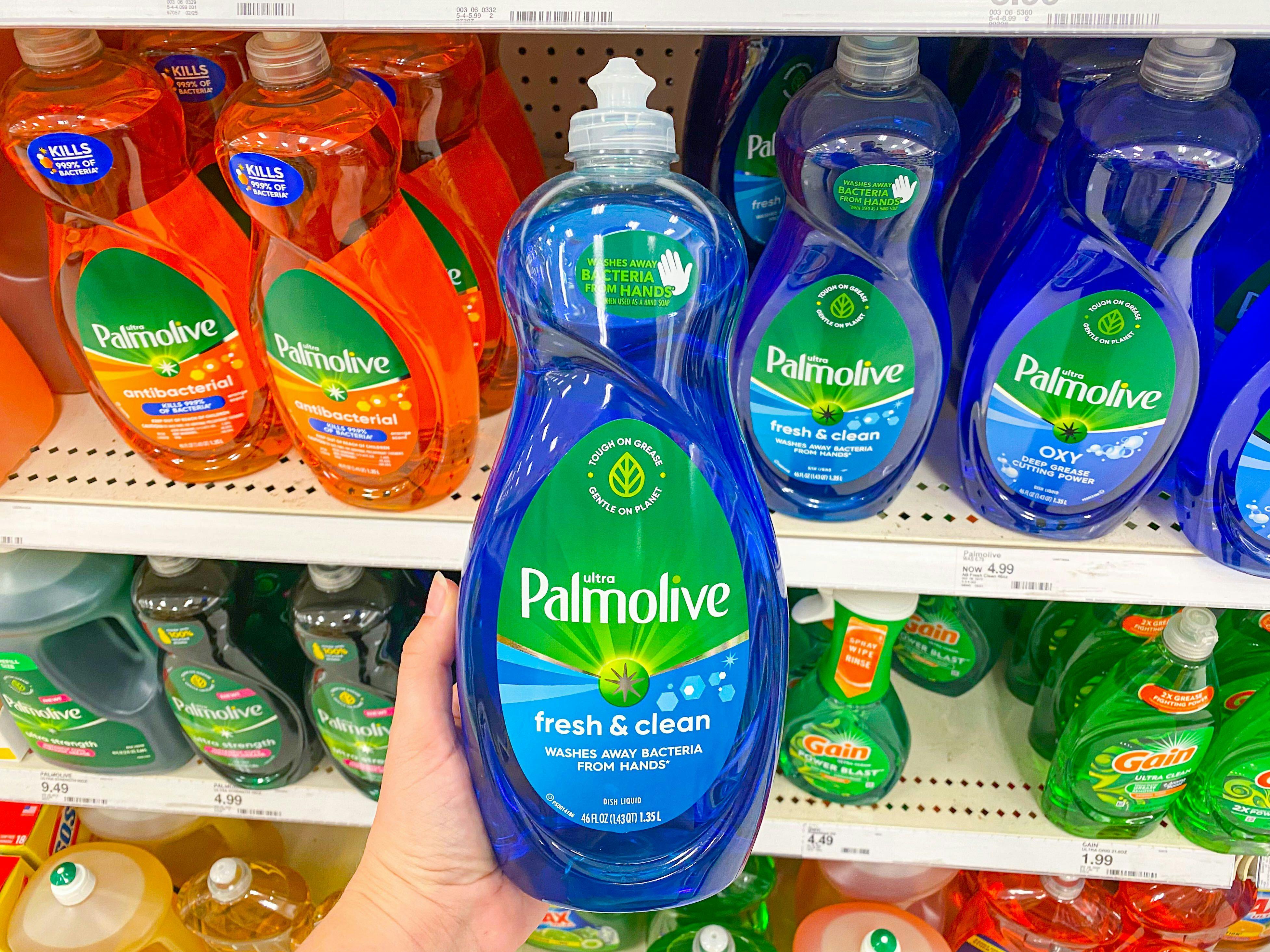 A person holding a bottle of Palmolive dish soap in front of a shelf of dish soap.