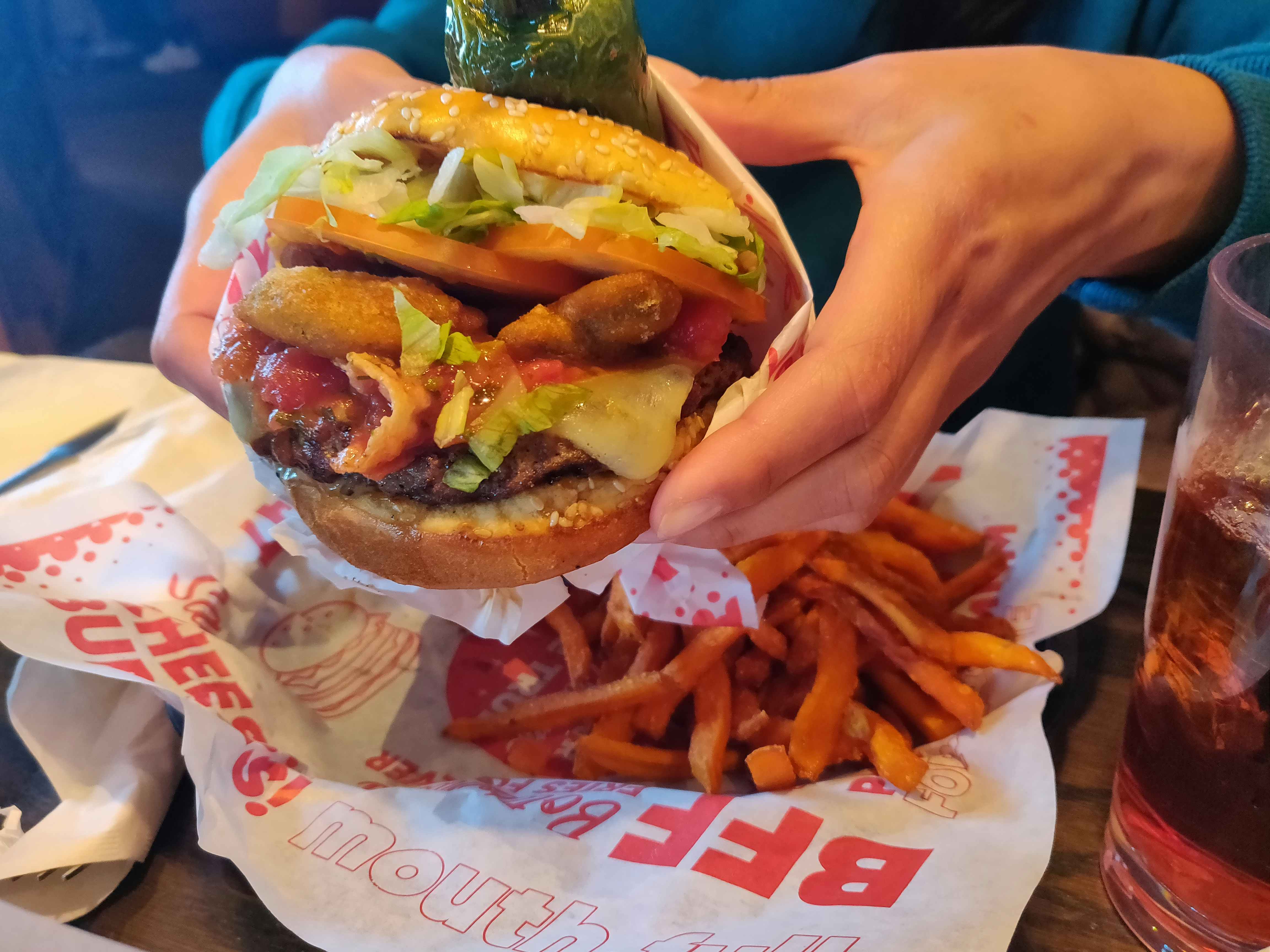 A person's hands holding a very large Jalapeño Burger from Red Robin over a basket with seasoned fries sitting on a table.