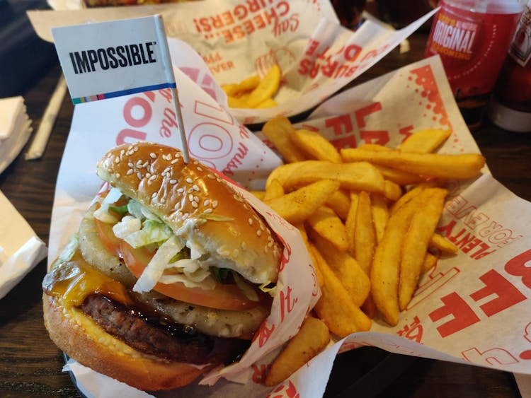A large impossible burger sitting in a Red Robin basket with some fries. A tiny flag that reads, 