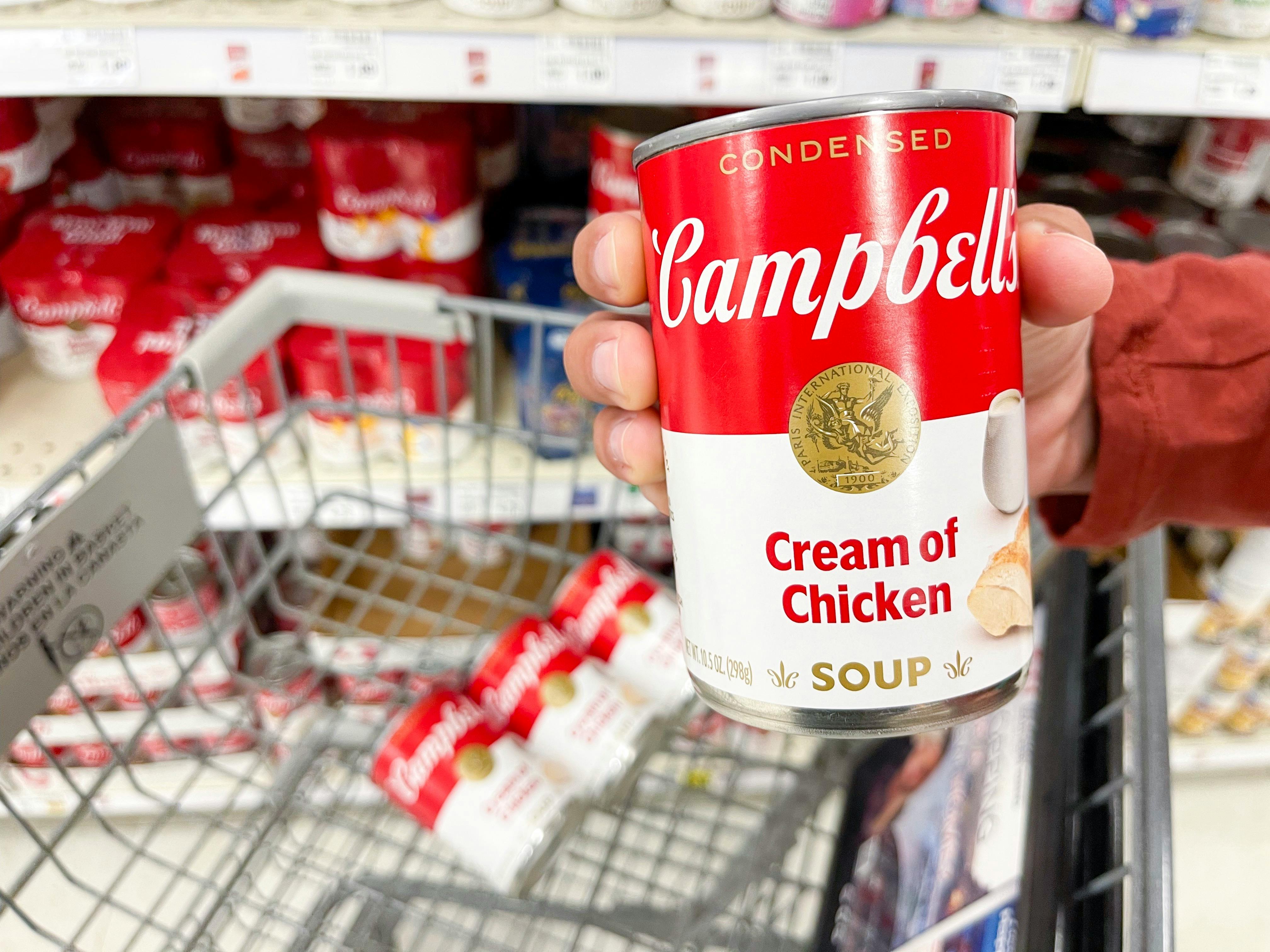 a person holding a can of soup along with other cans in cart