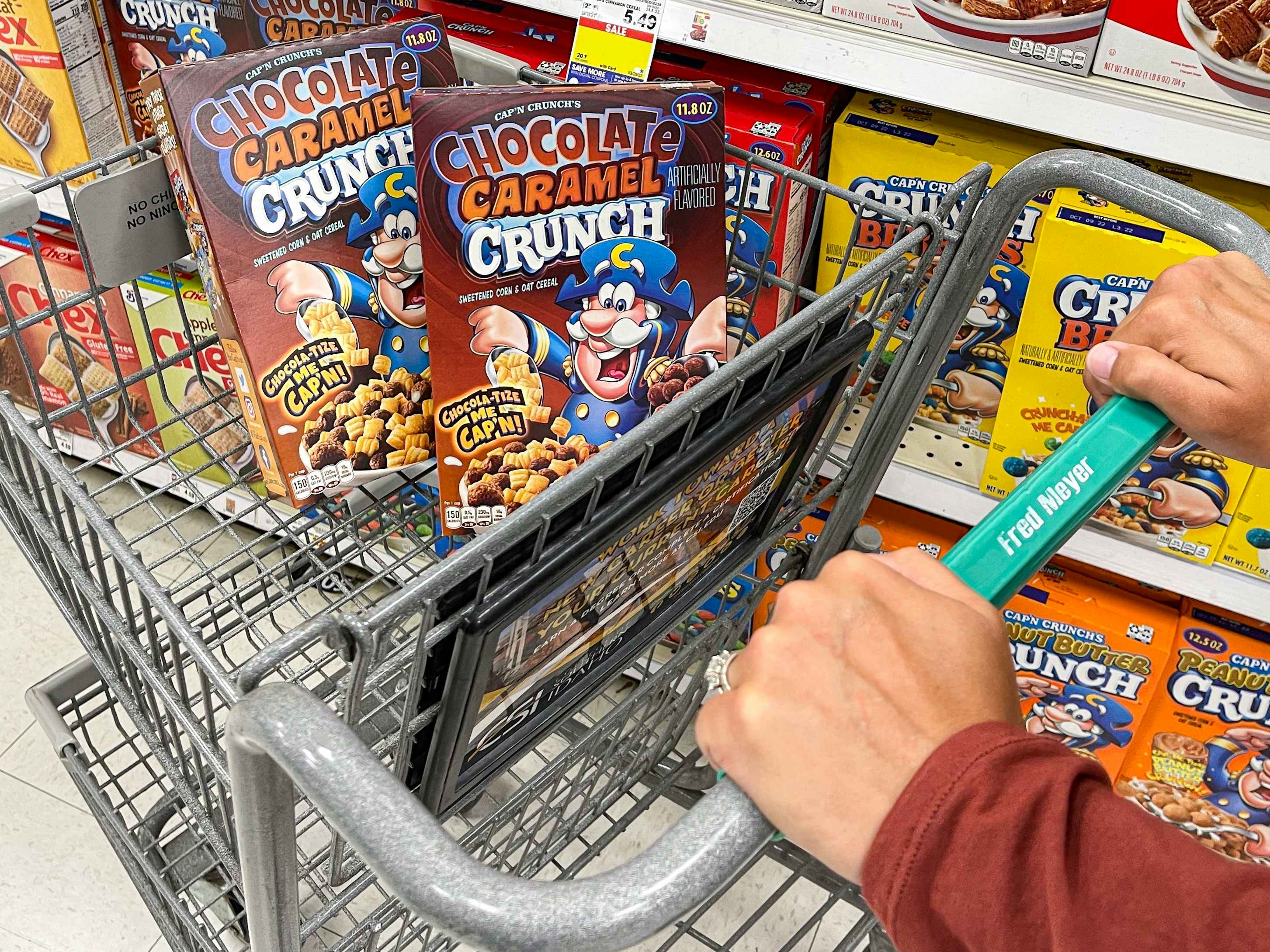 a person pushing a fred meyer cart with 2 boxes of capn crunch in basket