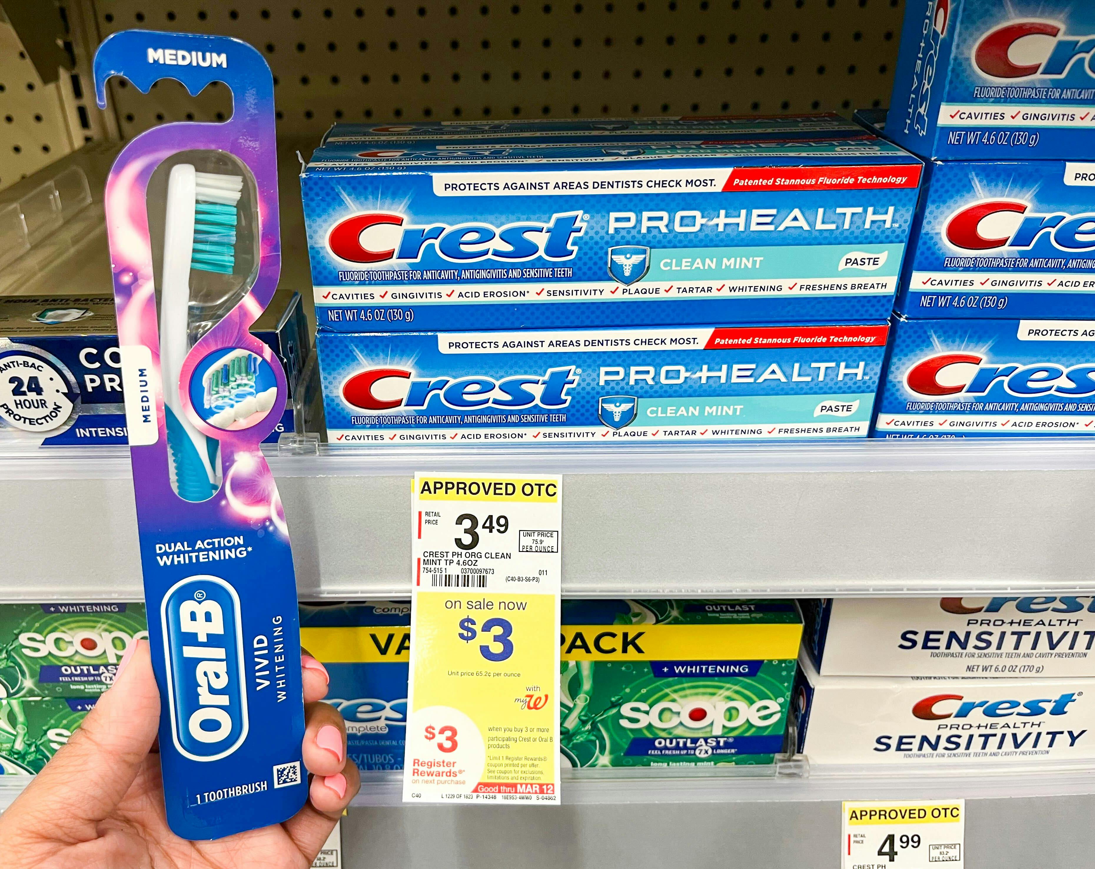 A person holding an oral-b toothbrush next to a shelf holding crest pro-health toothpaste