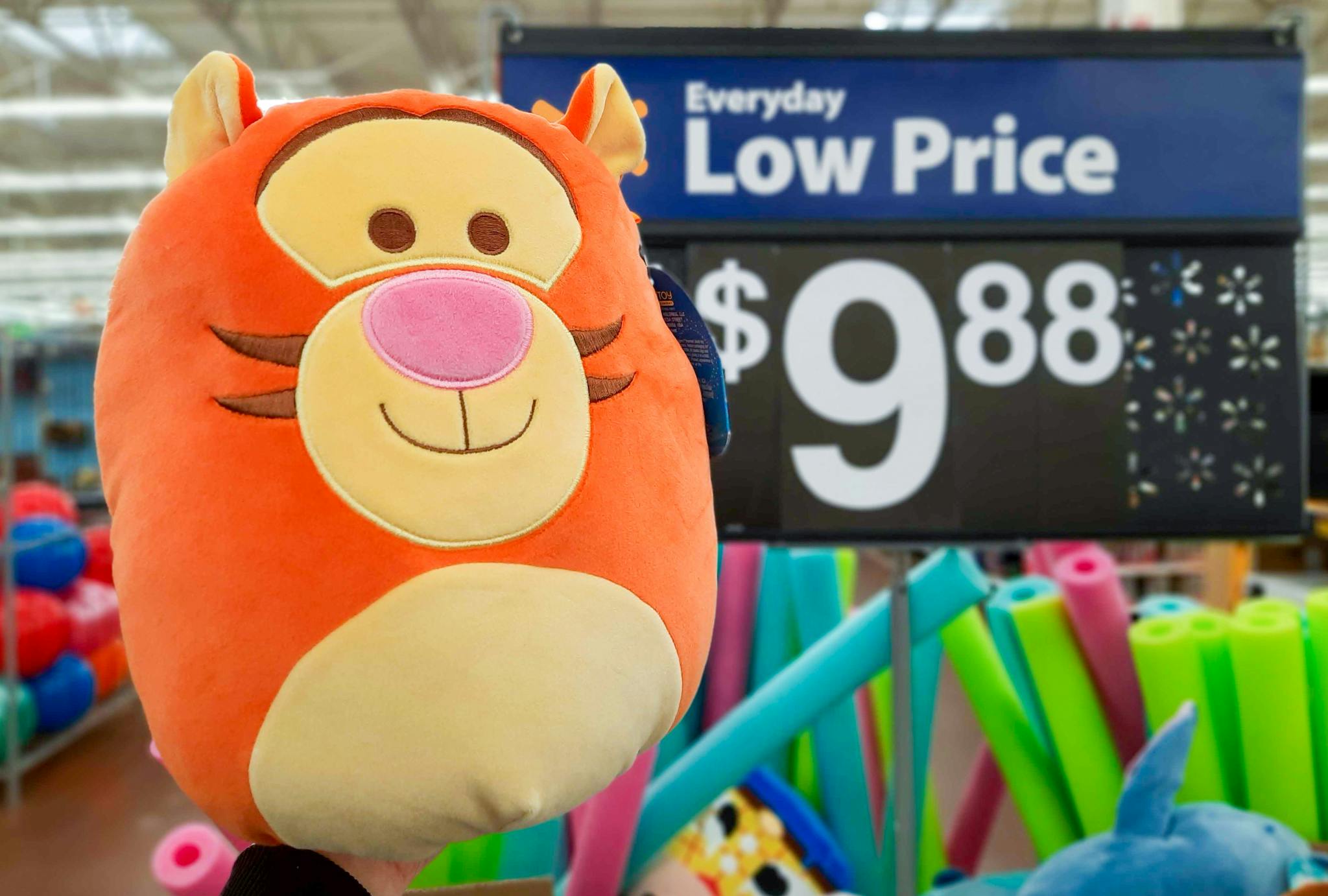 A Tigger Squishmallow being held up next to a Walmart sign showing the price to be $9.88