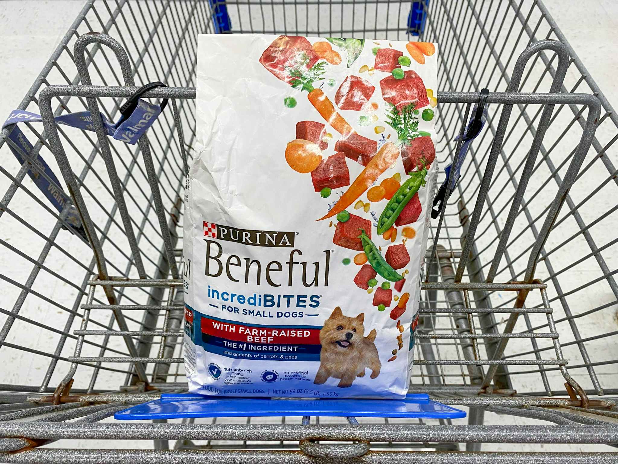 A bag of Purina Beneful incrediBITES for small dogs sitting in the basket of a Walmart shopping cart.