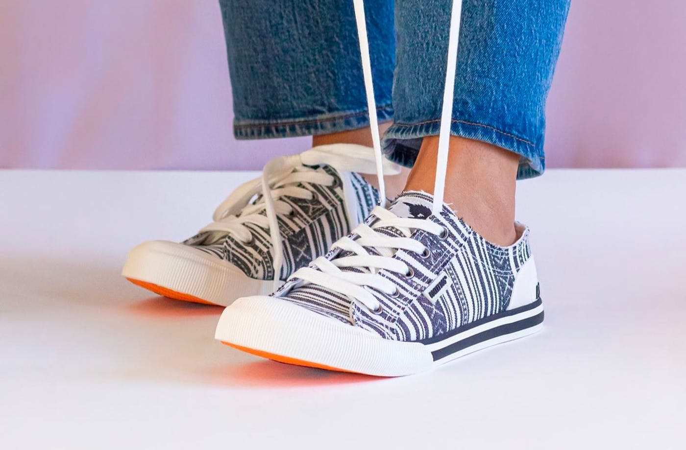 A pair of lace-up shoes on a persons feet. One shoes has the laces pulled straight up like they're going to be tied.