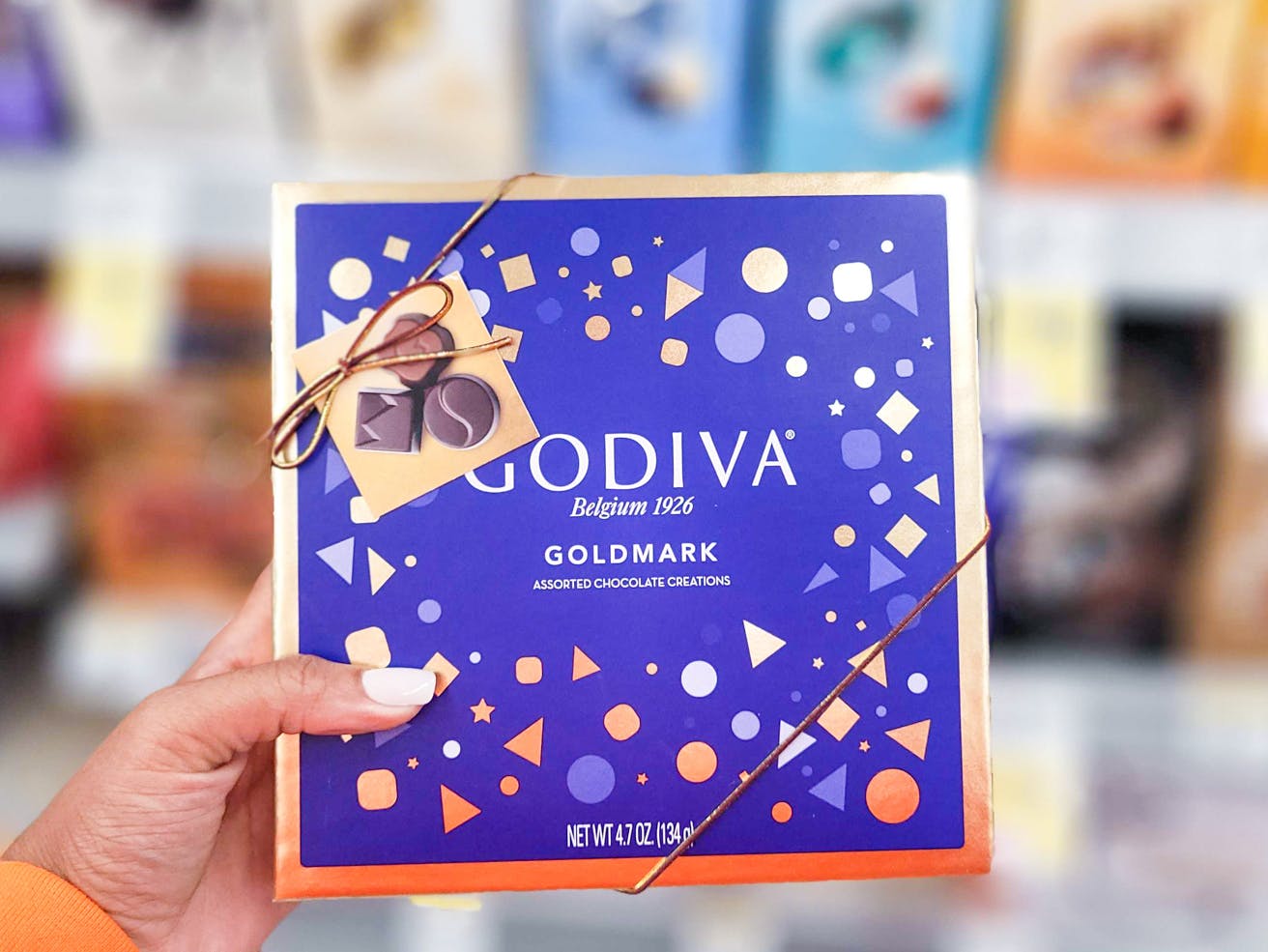 A person's hand holding a box of Godiva assorted chocolates.