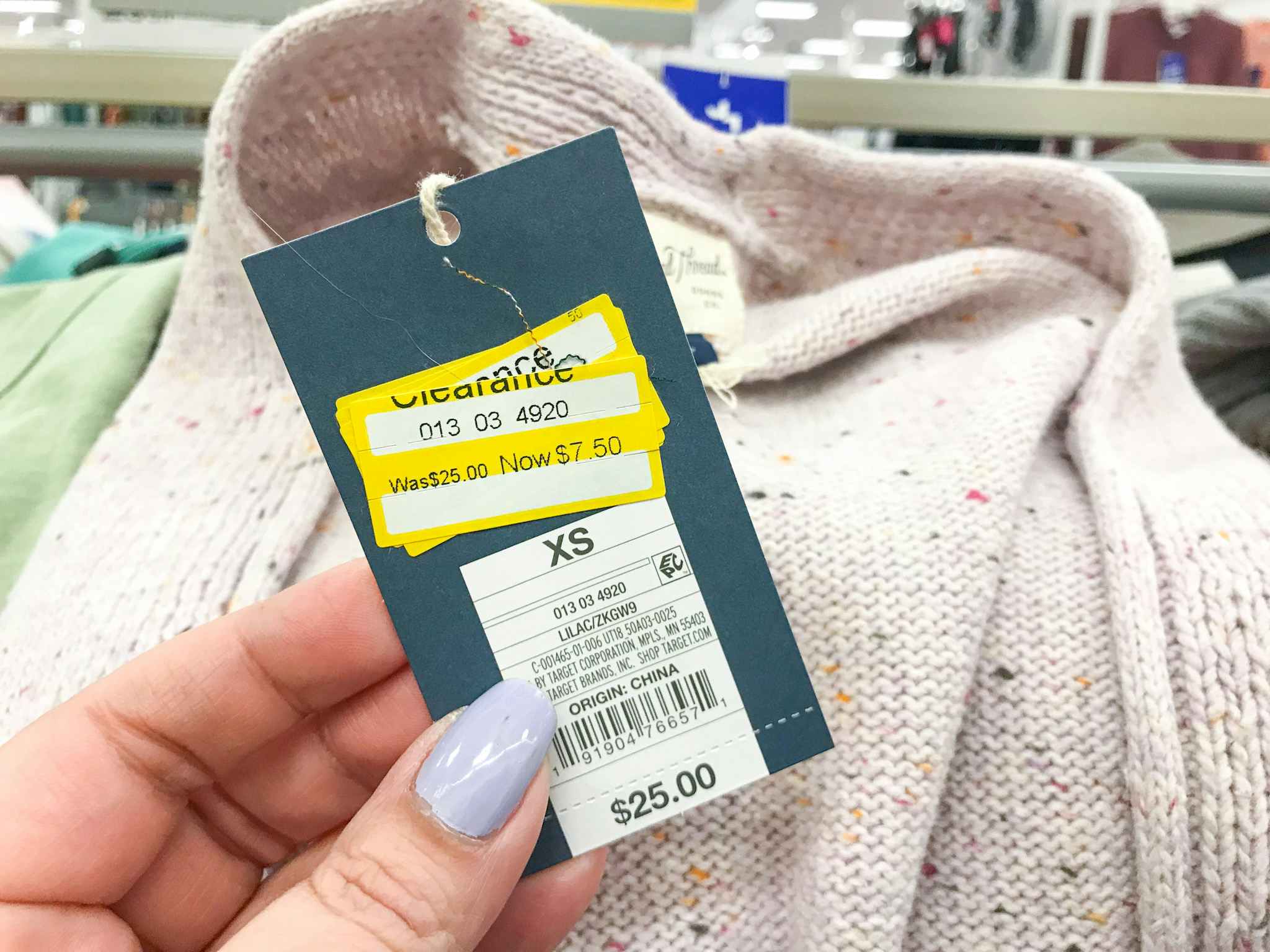 woman's hand holding up clearance price tag on an XS sweater
