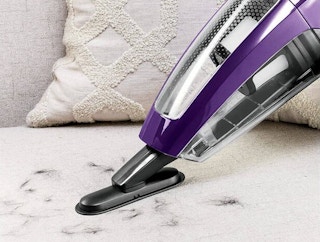 A vaccuum being used on a couch with dog hair on it.