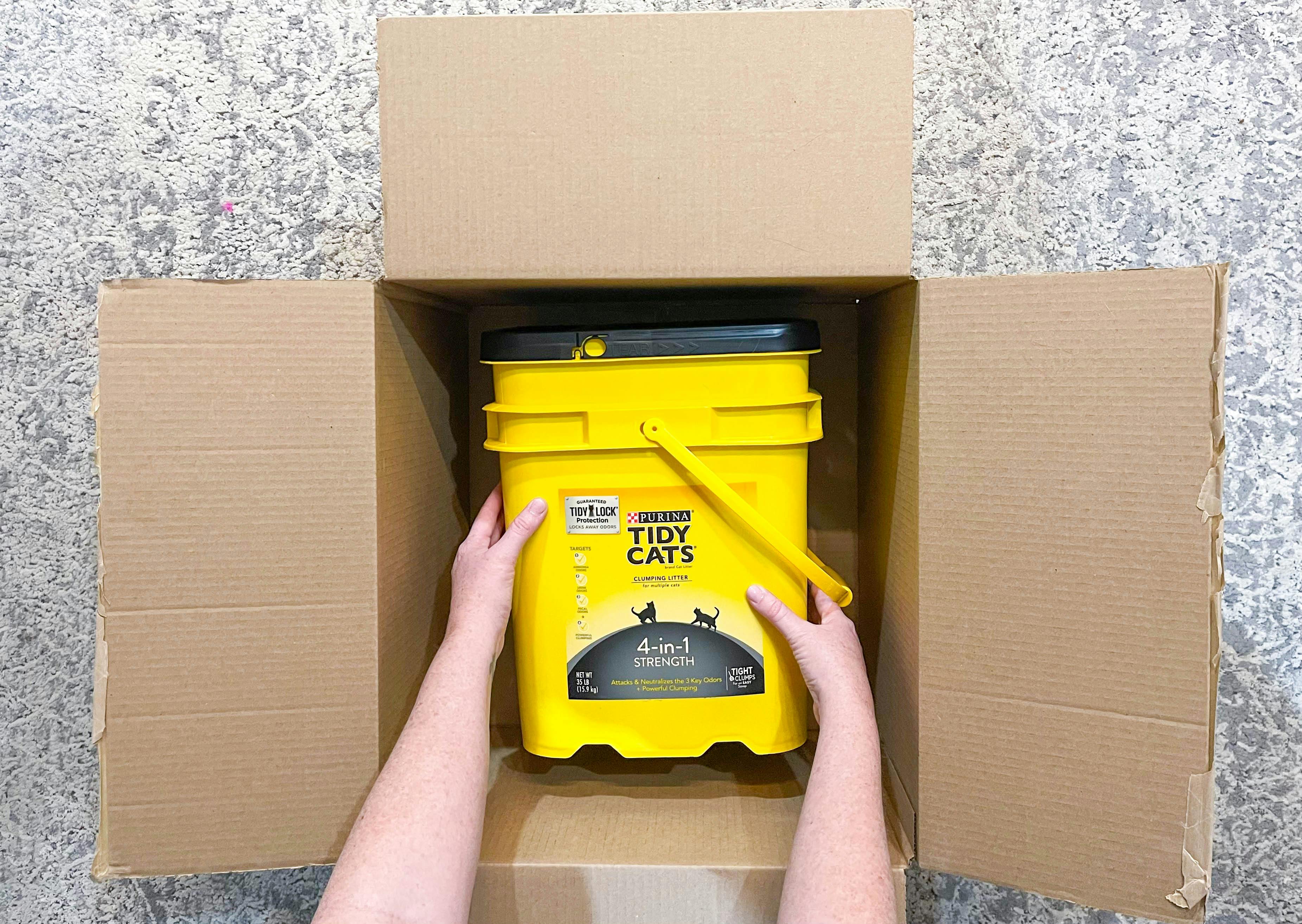 a person pulling out a container of cat litter out of a box