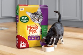 sam's club exclusive mixture meow mix food near a cat eating from a bowl