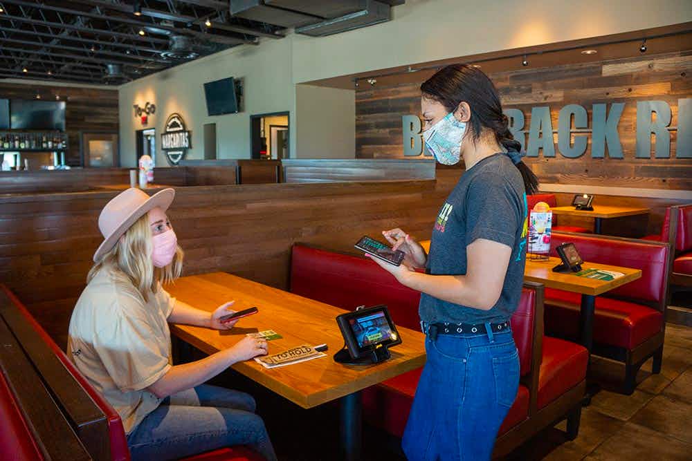 A Chili's employee taking an order for a customer sitting in a booth at Chili's.