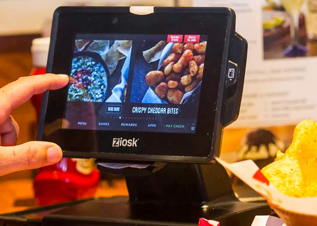 A person's hand reaching to use the Ziosk tablet on a table at Chili's.