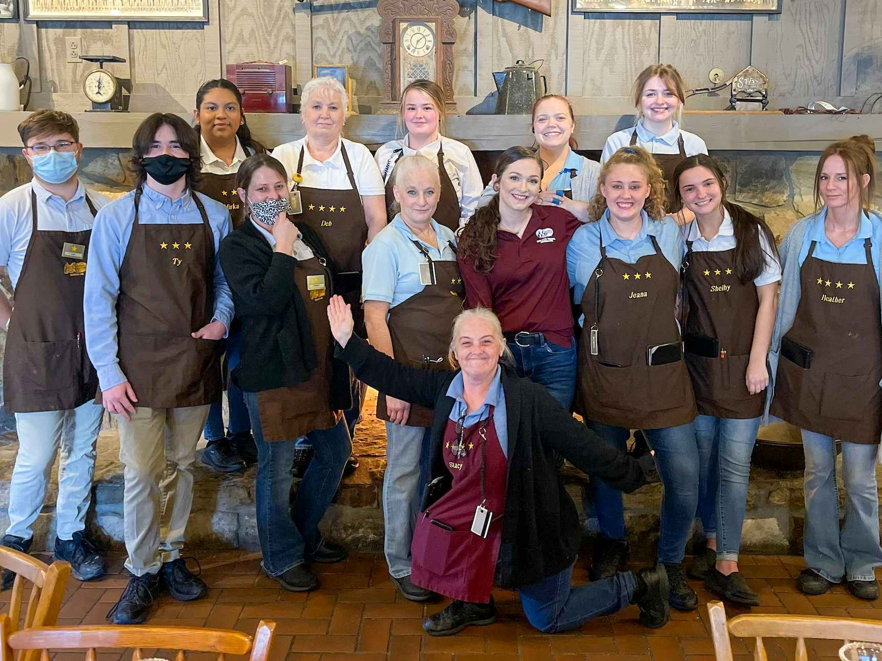 A group of Cracker Barrel employees posing in front of a Cracker Barrel fireplace. 