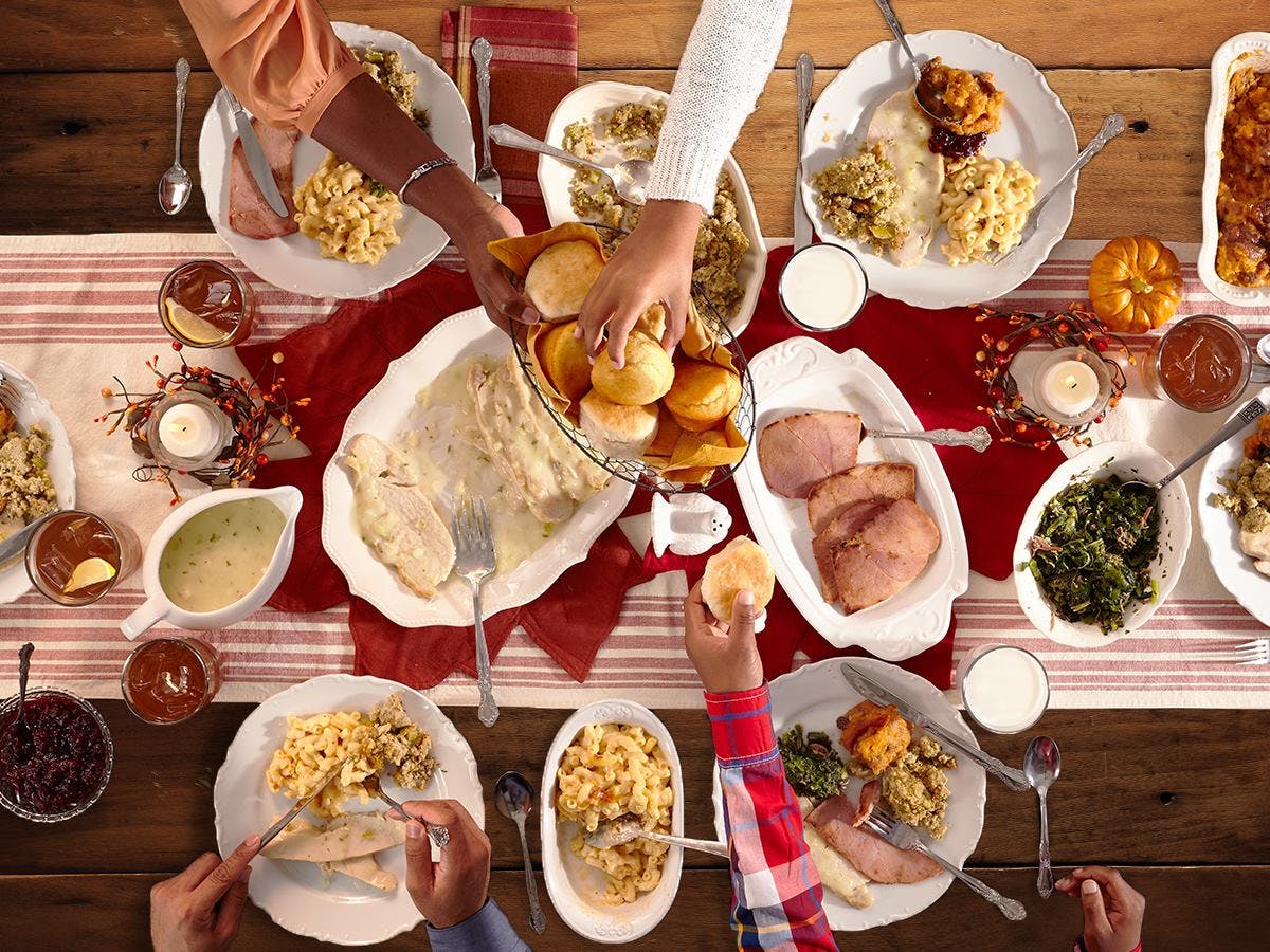 Thanksgiving meal laid out on a table with hands reaching to grab food.