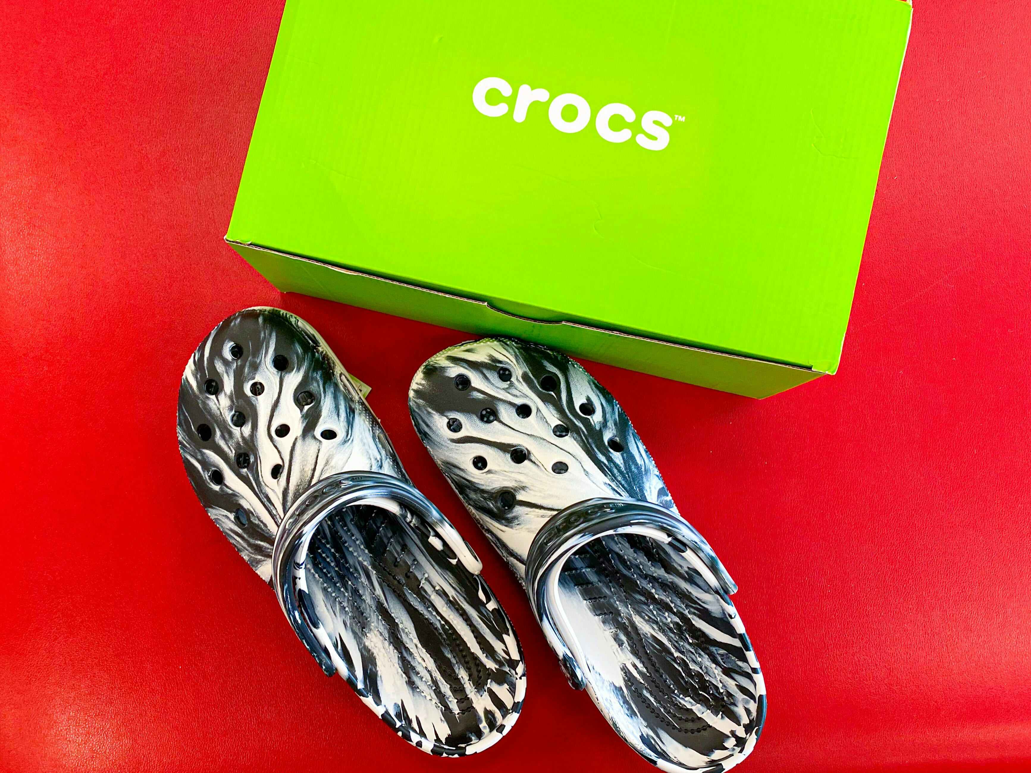 crocs clogs next to a green crocs box on a red surface