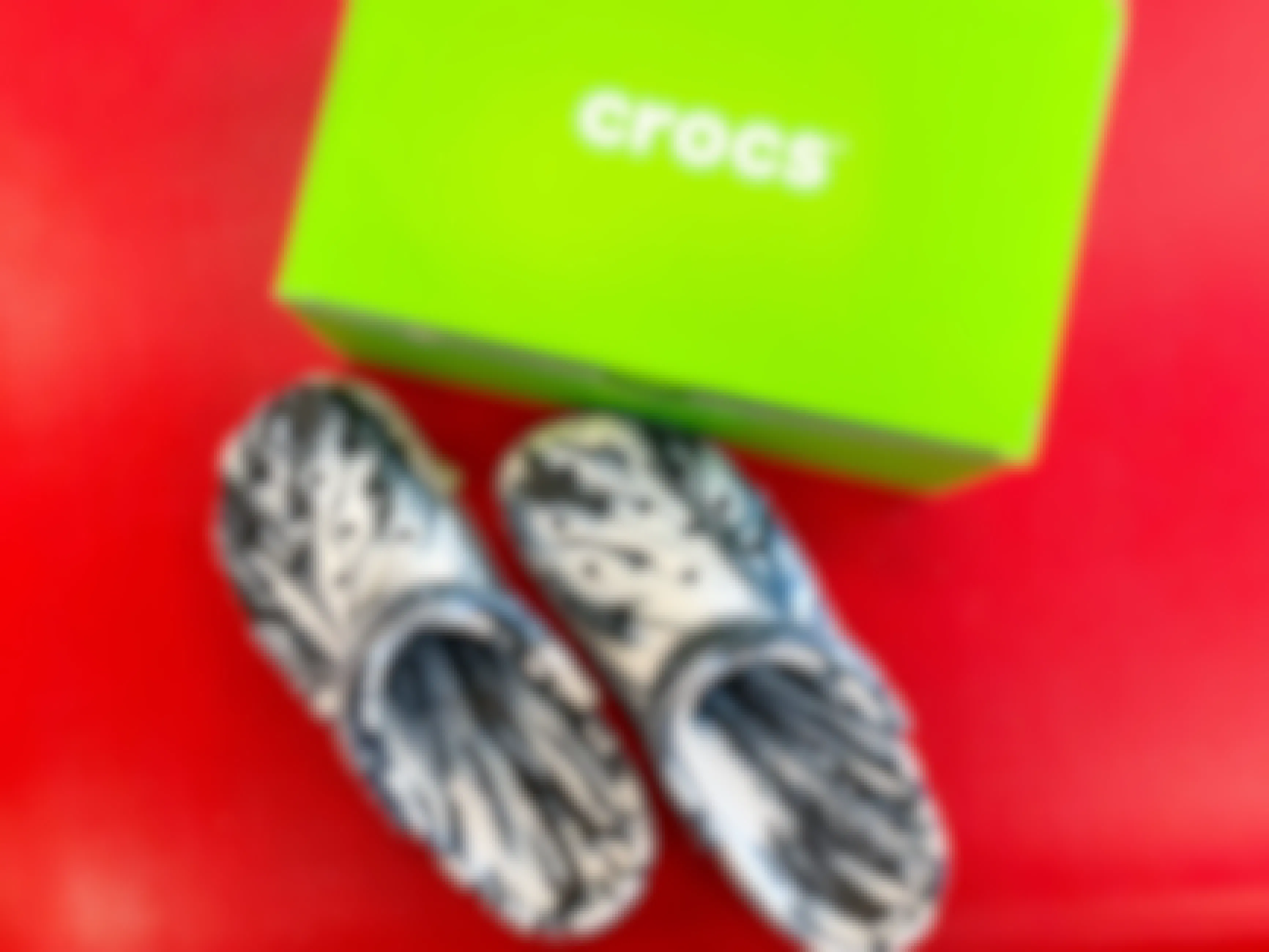 crocs clogs next to a green crocs box on a red surface