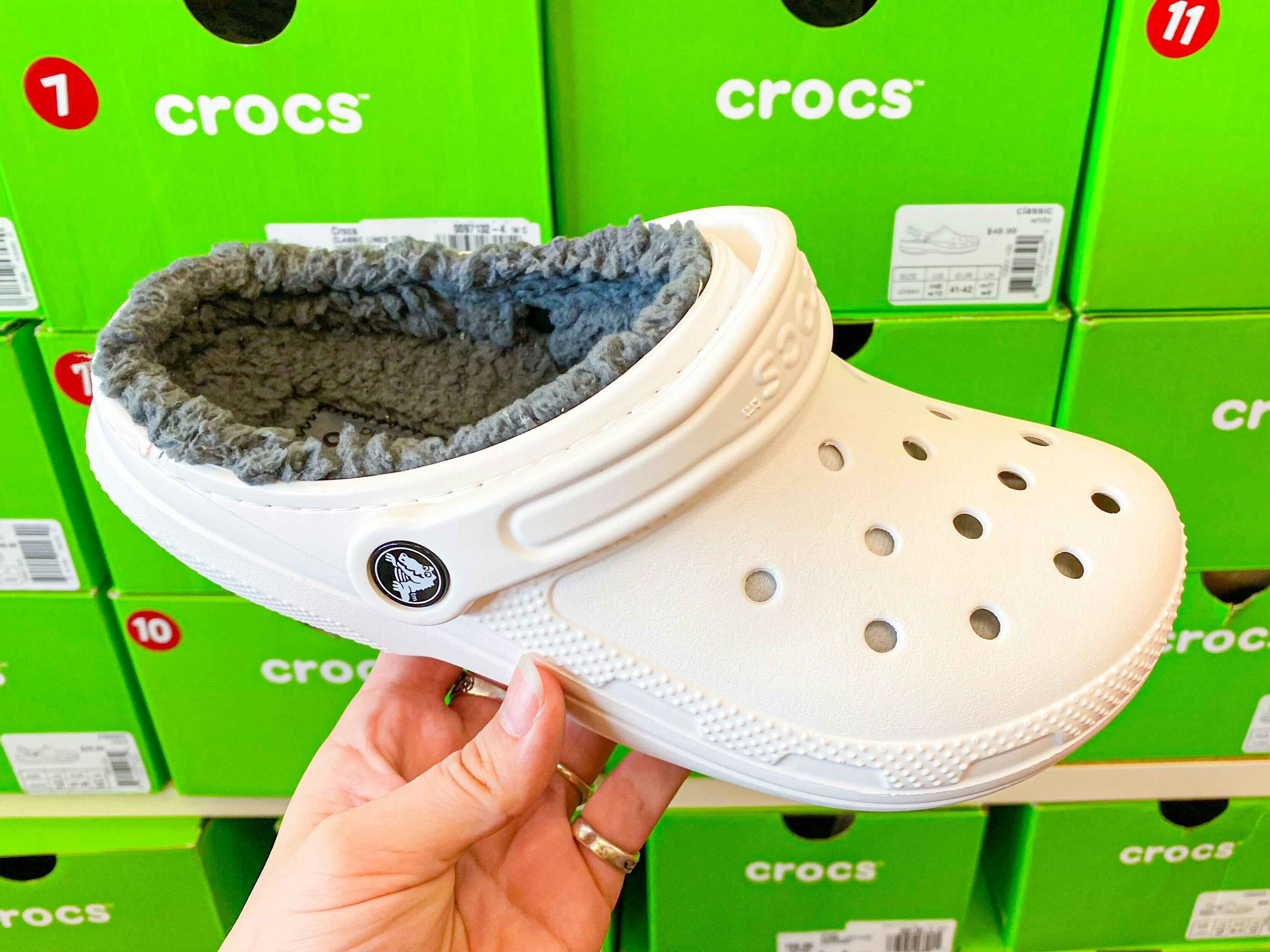 A person's hand holding a fuzzy Croc clog in a shoe store.