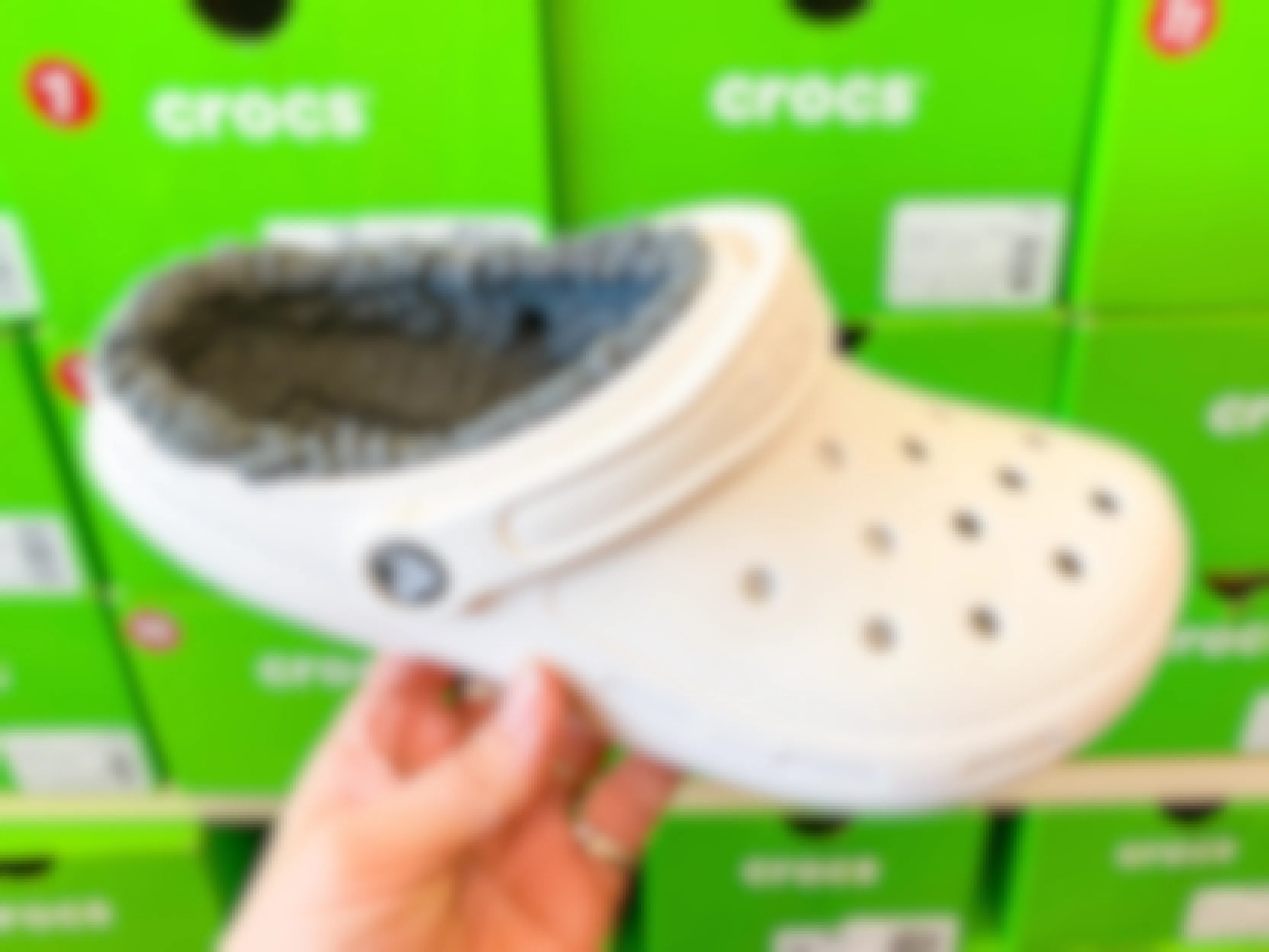 A person's hand holding a fuzzy Croc clog in a shoe store.
